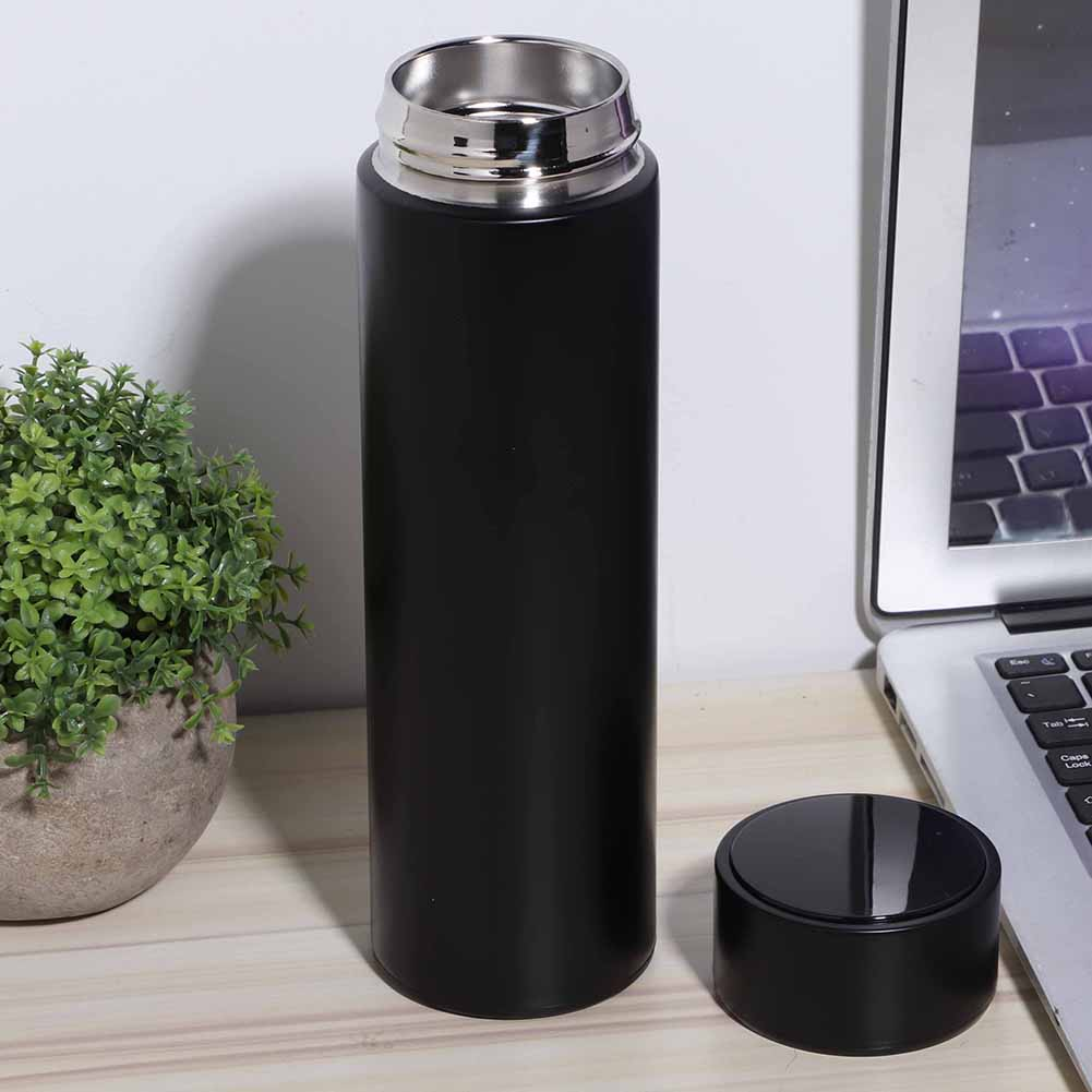 Eine schwarze isolierte Wasserflasche, Deckel ab, neben einem Laptop und einer kleinen Topfpflanze auf einer Holzoberfläche.