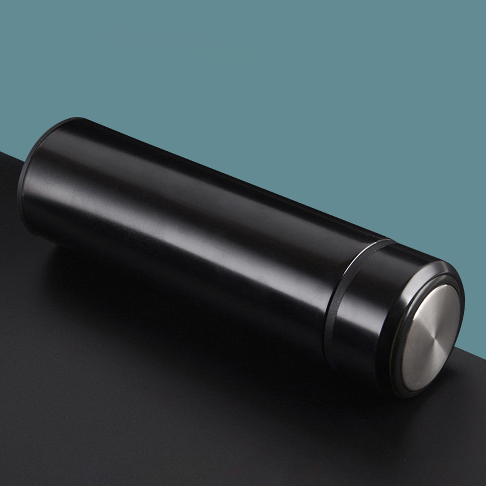 Eine schwarze isolierte Wasserflasche liegt auf einer schwarzen Oberfläche vor teal Hintergrund. Der Deckel ist silber.