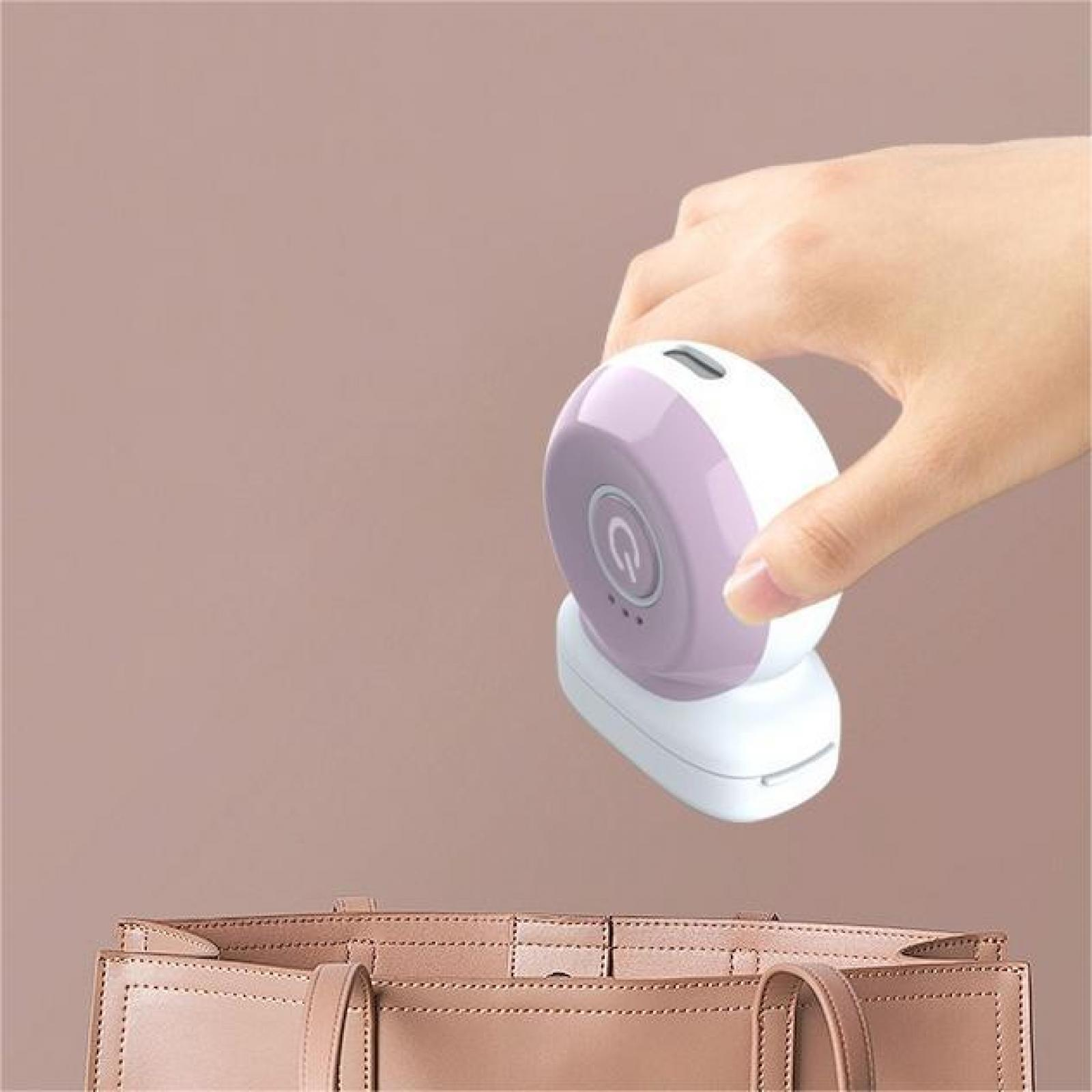Eine Hand hält ein weißes und lila Gerät über einer Handtasche. Das Gerät hat einen Ein-/Ausschalter.
