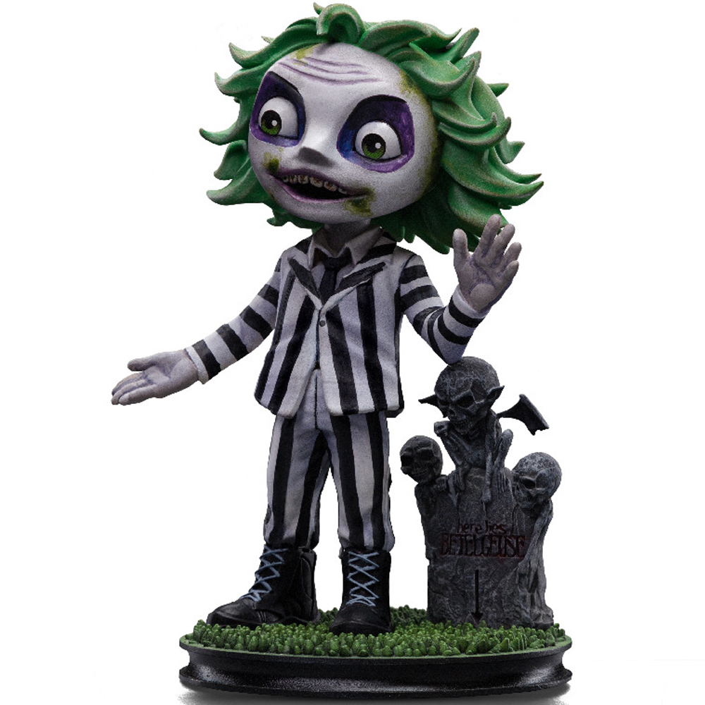 Statuetta di Beetlejuice con capelli verdi, abito a righe bianche e nere. Una lapide con teschi sullo sfondo.
