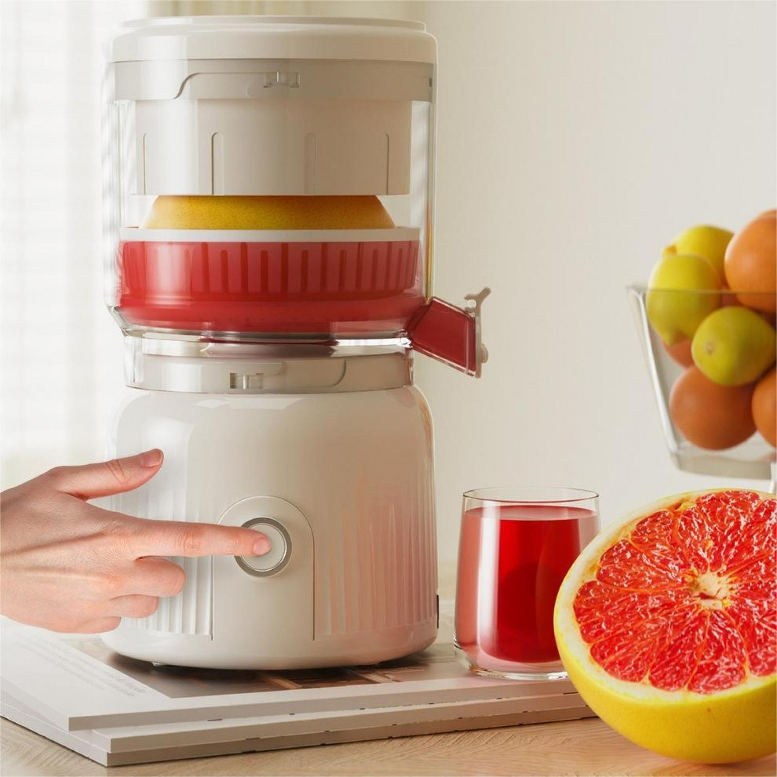 Ein Finger drückt einen Entsafterknopf. Ein Glas Saft, eine Grapefruit-Hälfte und Obst sind ebenfalls sichtbar.