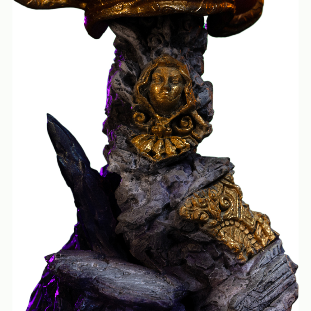 Eine Statue mit Steinsockel, goldfarbenem Gesicht und goldenen Verzierungen. Die Statue wird von violettem Licht beleuchtet.