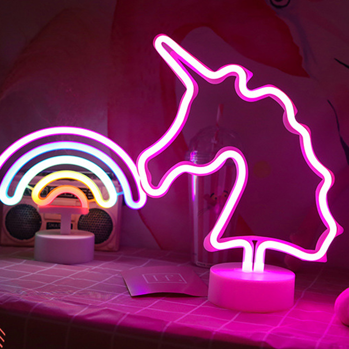 Eine Neon-Einhorn- und Regenbogenlampe. Die Lampen sind rosa und weiß. Der Hintergrund ist eine rosa Oberfläche mit einem Retro-Radio.