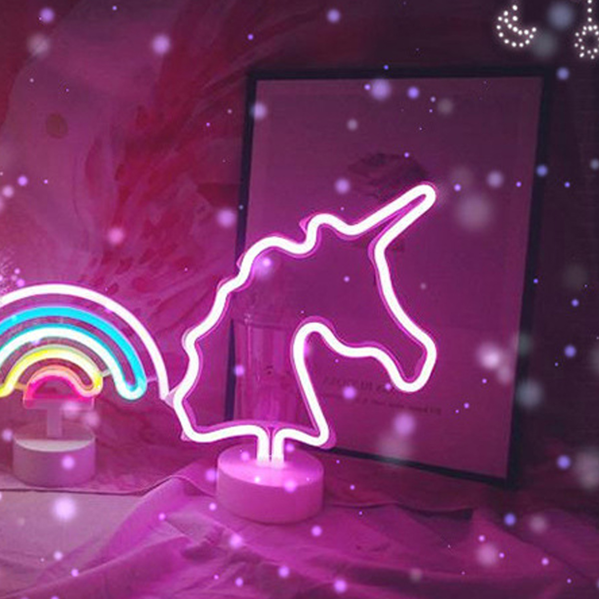 Neonlichter eines Einhorns und Regenbogens. Rosa und weiße Lichter auf pinkfarbenem Hintergrund. Ein gerahmtes Bild befindet sich hinter dem Einhorn.