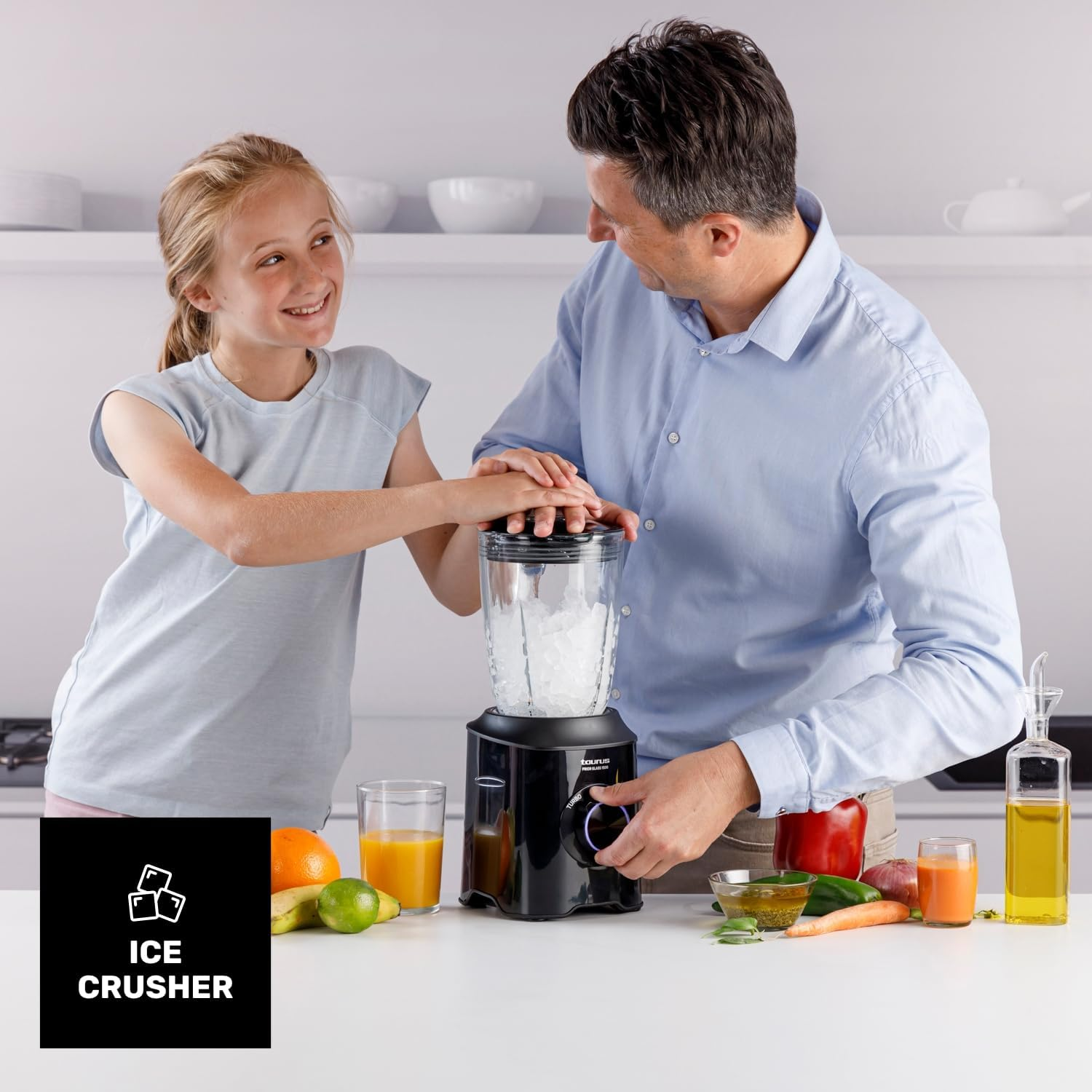 Un hombre y una niña usan una licuadora con hielo. Frutas y verduras están en la mesa.