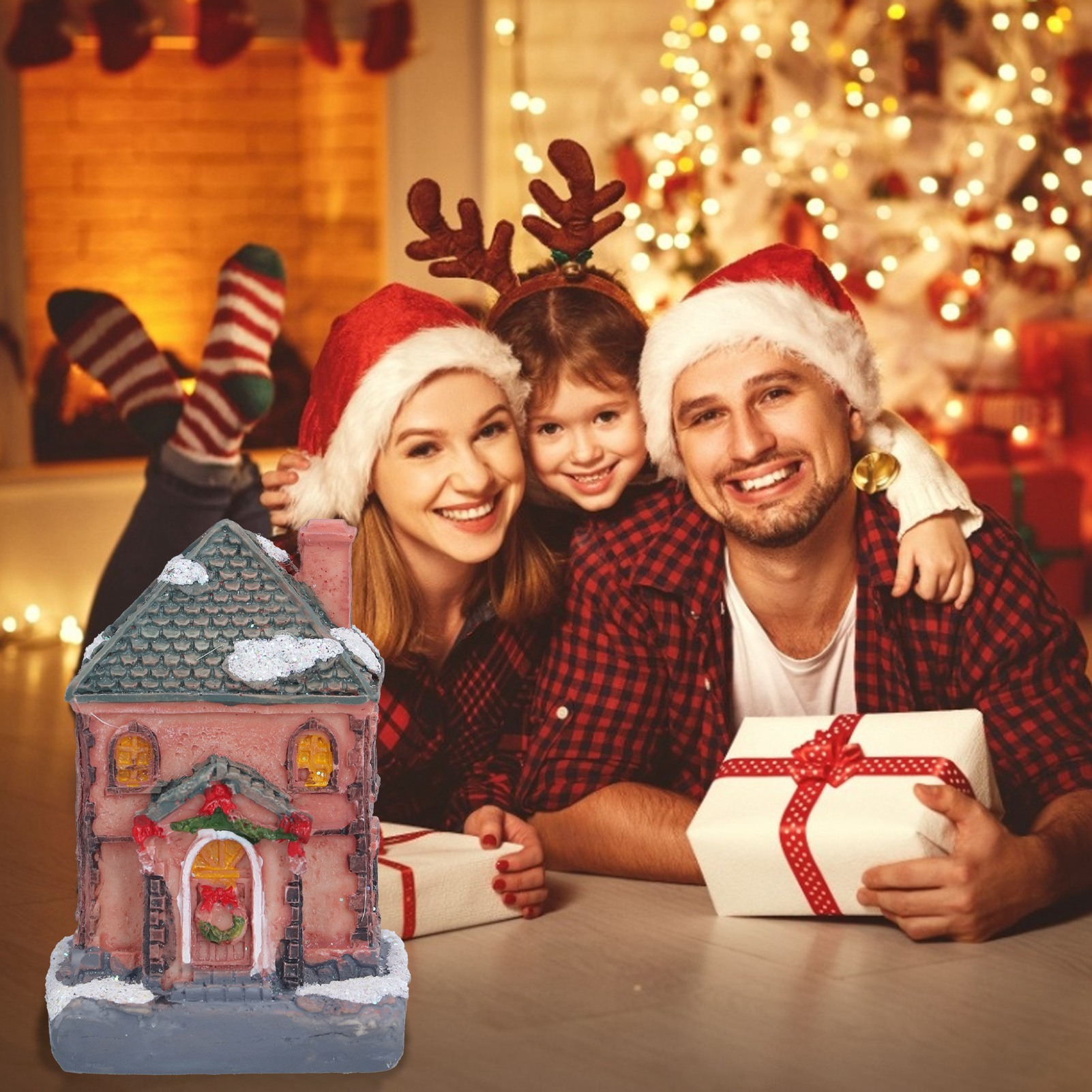 Familie mit Weihnachtsmützen, Weihnachtsbaum im Hintergrund, Geschenkbox. Ein kleines Haus im Vordergrund.