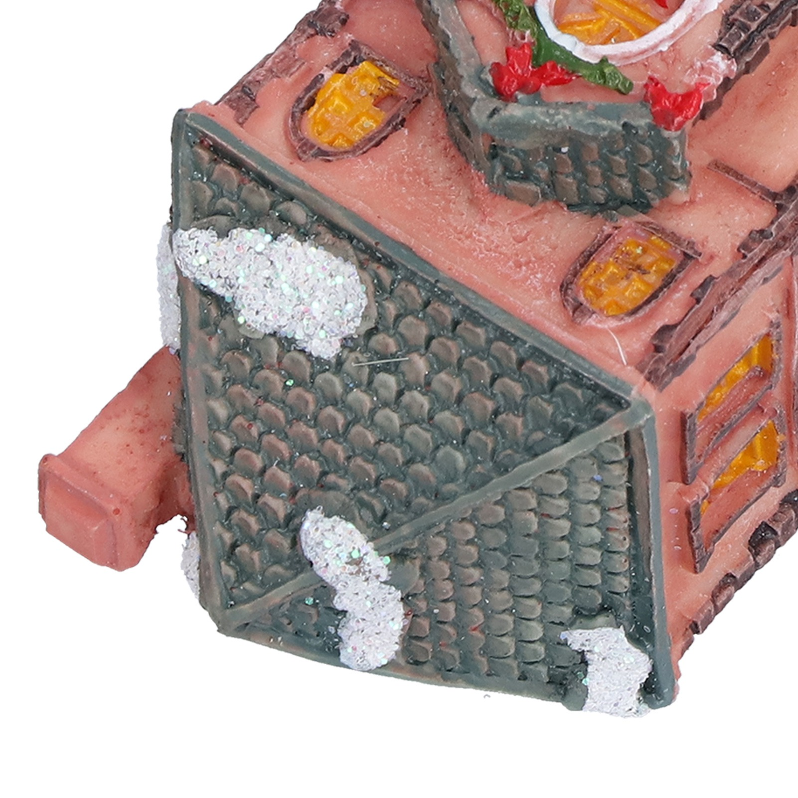 Ein Miniaturhaus mit grünem Dach, rosa Wänden und gelben Fenstern, bedeckt mit glitzerndem weißem Schnee.