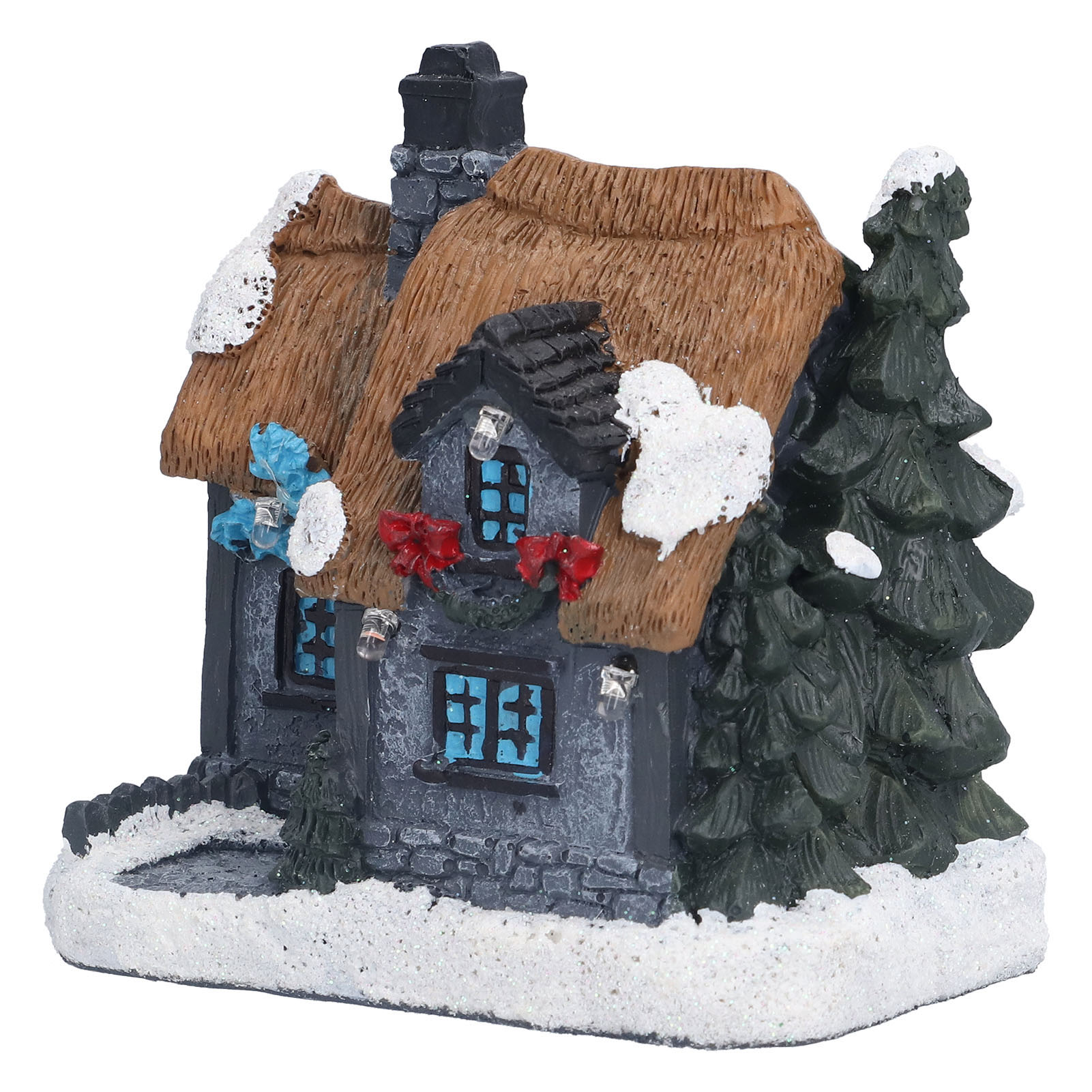 Ein Miniatur-Weihnachtshaus mit Strohdach, Schnee und einem Tannenbaum. Es hat blaue Fenster und rote Schleifen.