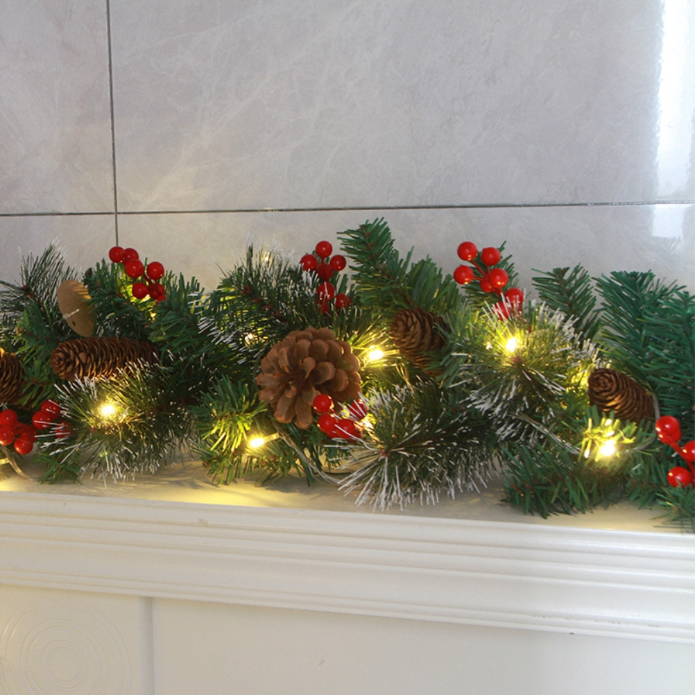 Weihnachtsgirlande mit Tannenzapfen, roten Beeren und Lichtern auf einem weißen Kaminsims. Der Hintergrund ist eine weiße Fliesenwand.