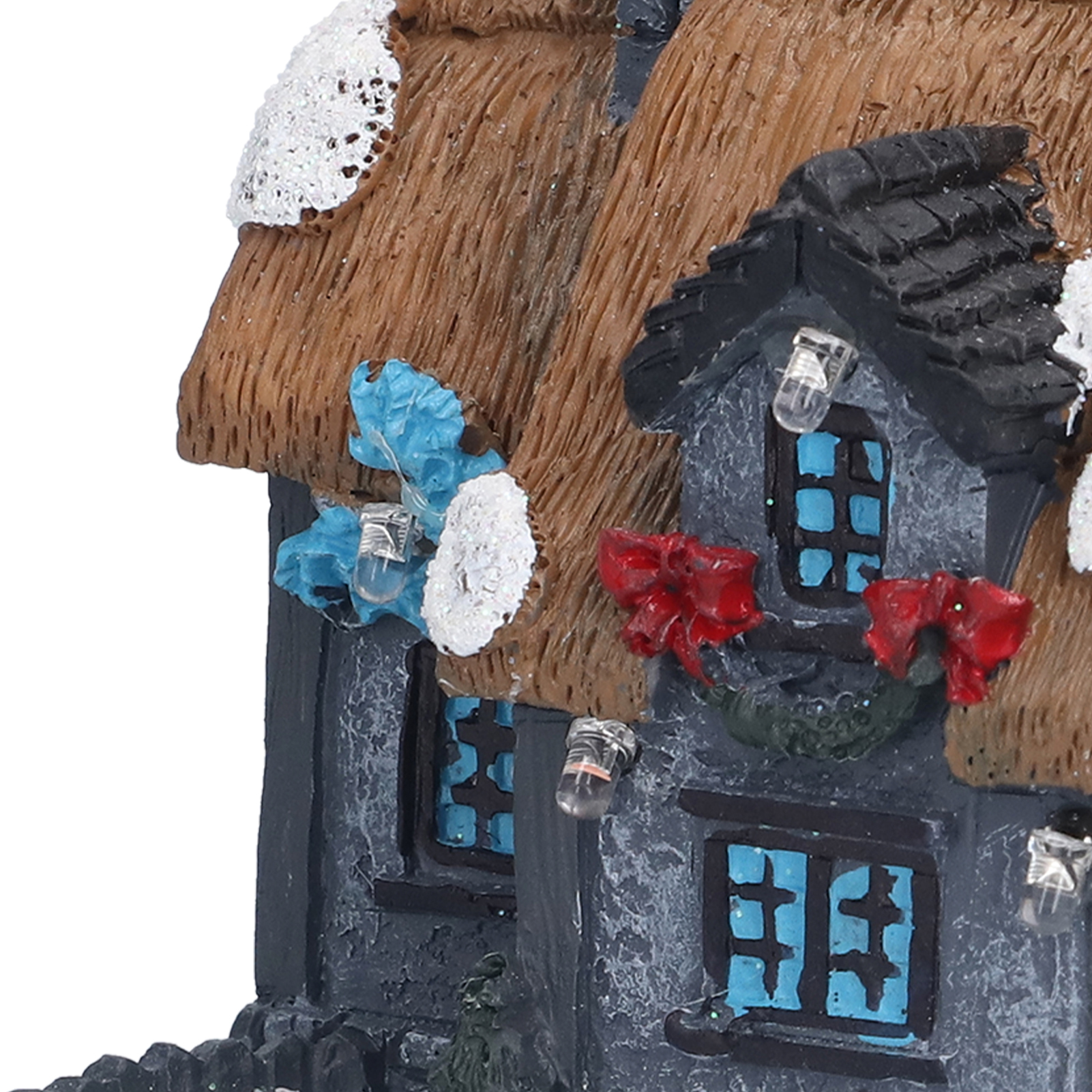 Ein Miniaturhaus mit Strohdach und Schnee. Es hat blaue Fenster, rote Schleifen und dekorative Lichter.