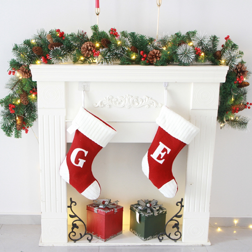 Ein weißer Kamin mit Weihnachtsstrümpfen, Girlanden und Geschenken. Rote Strümpfe mit den Buchstaben G und E. Geschenke liegen unter dem Kamin.