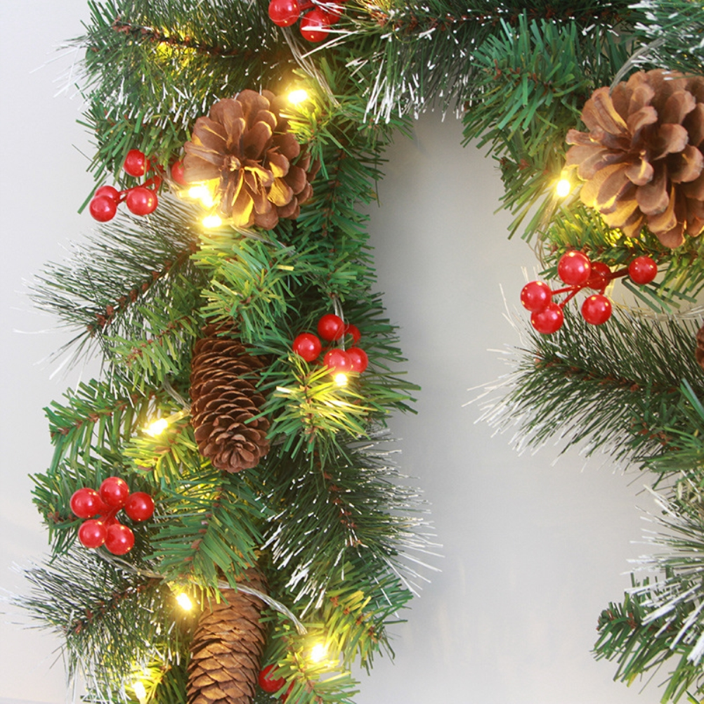 Nahaufnahme eines Weihnachtskranzes mit Tannenzapfen, roten Beeren und Lichtern. Grüne Nadeln sind mit weißem Frost akzentuiert.