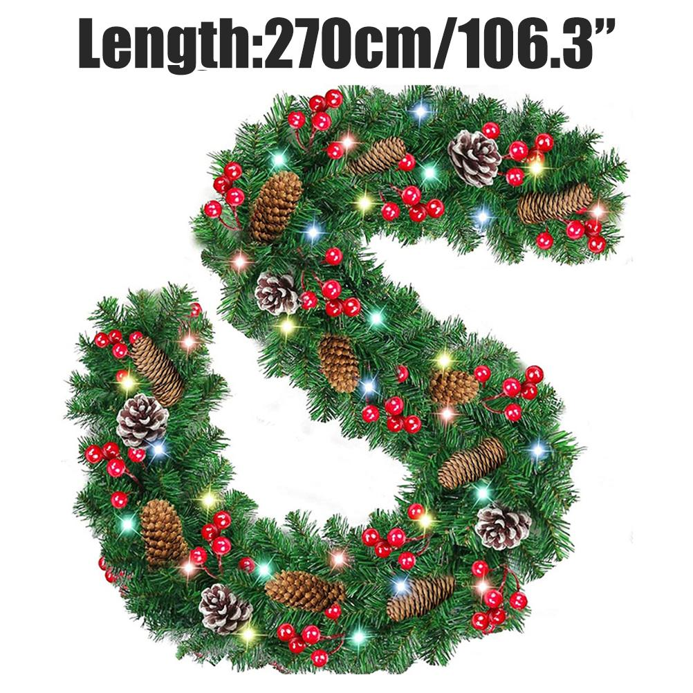 Ein grüner Weihnachtskranz mit roten Beeren, Tannenzapfen und kleinen Lichtern. Der Kranz hat die Form eines Buchstaben S.