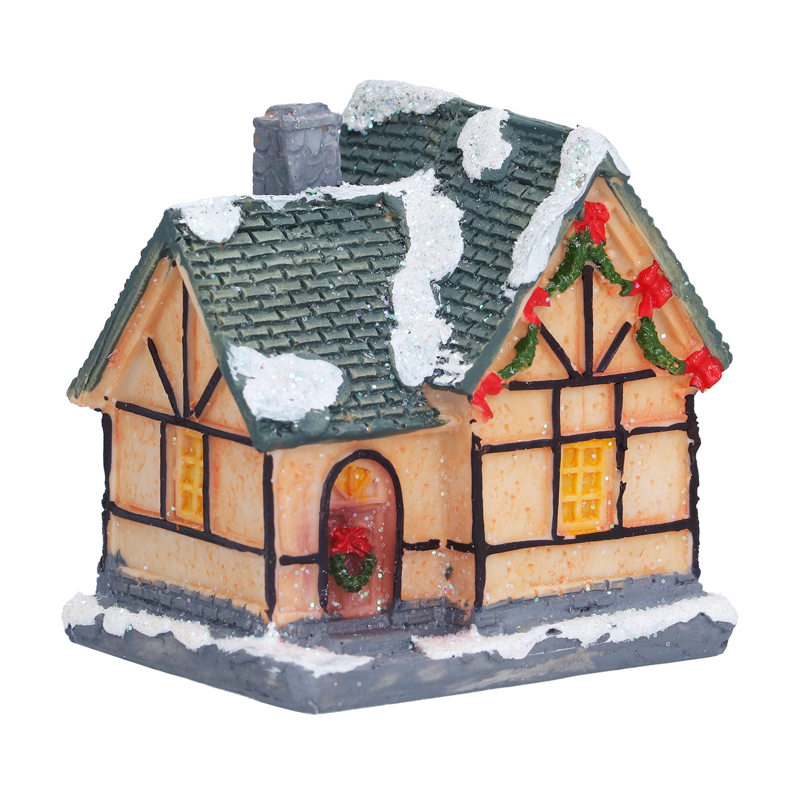 Ein Miniaturhaus mit grünem, schneebedecktem Dach, Schornstein und Weihnachtsdekorationen. Fenster und eine Tür sind sichtbar.