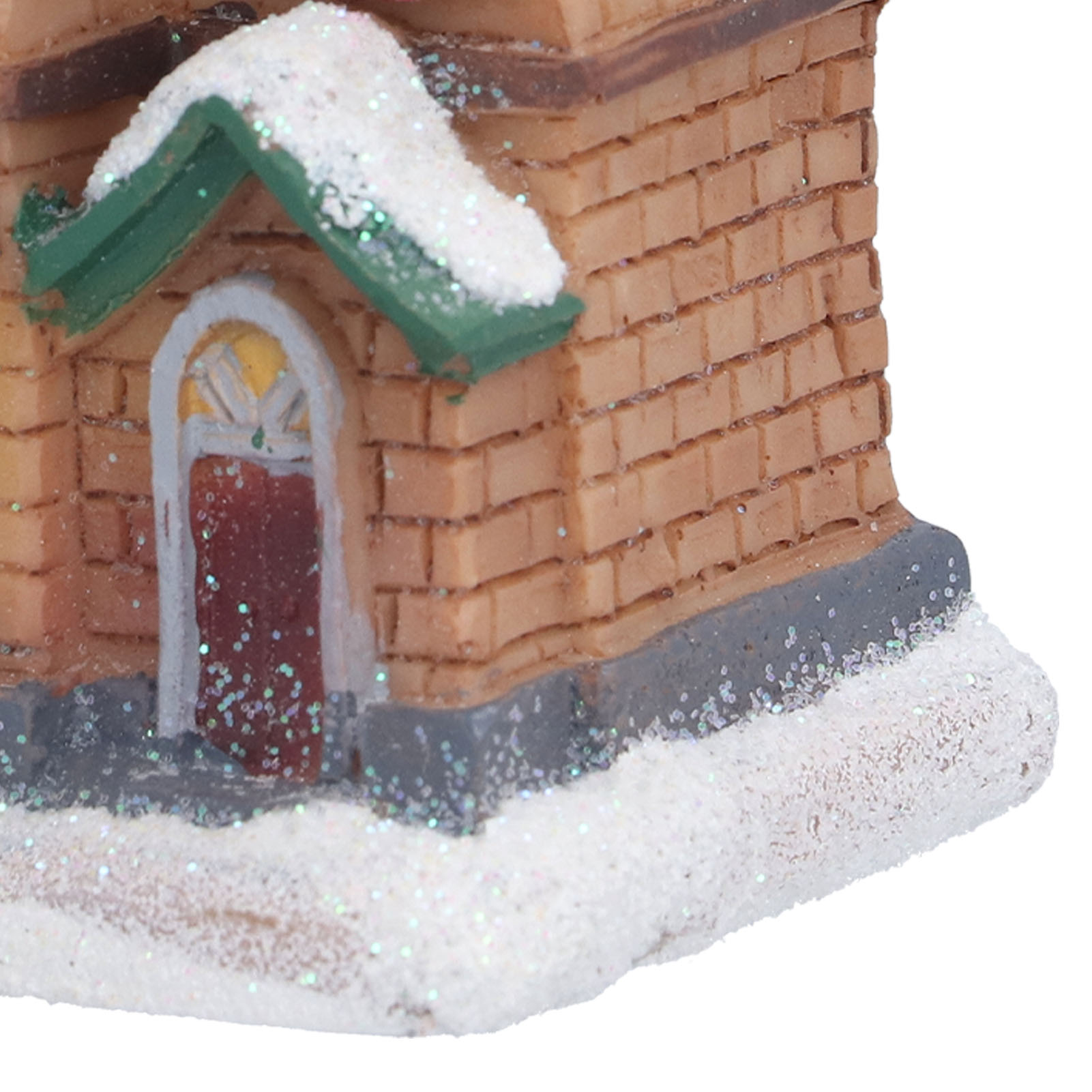 Ein Miniatur-Backsteinhaus mit grünem Dach und Schnee. Eine rote Tür ist sichtbar. Die Szene ist festlich und winterlich.