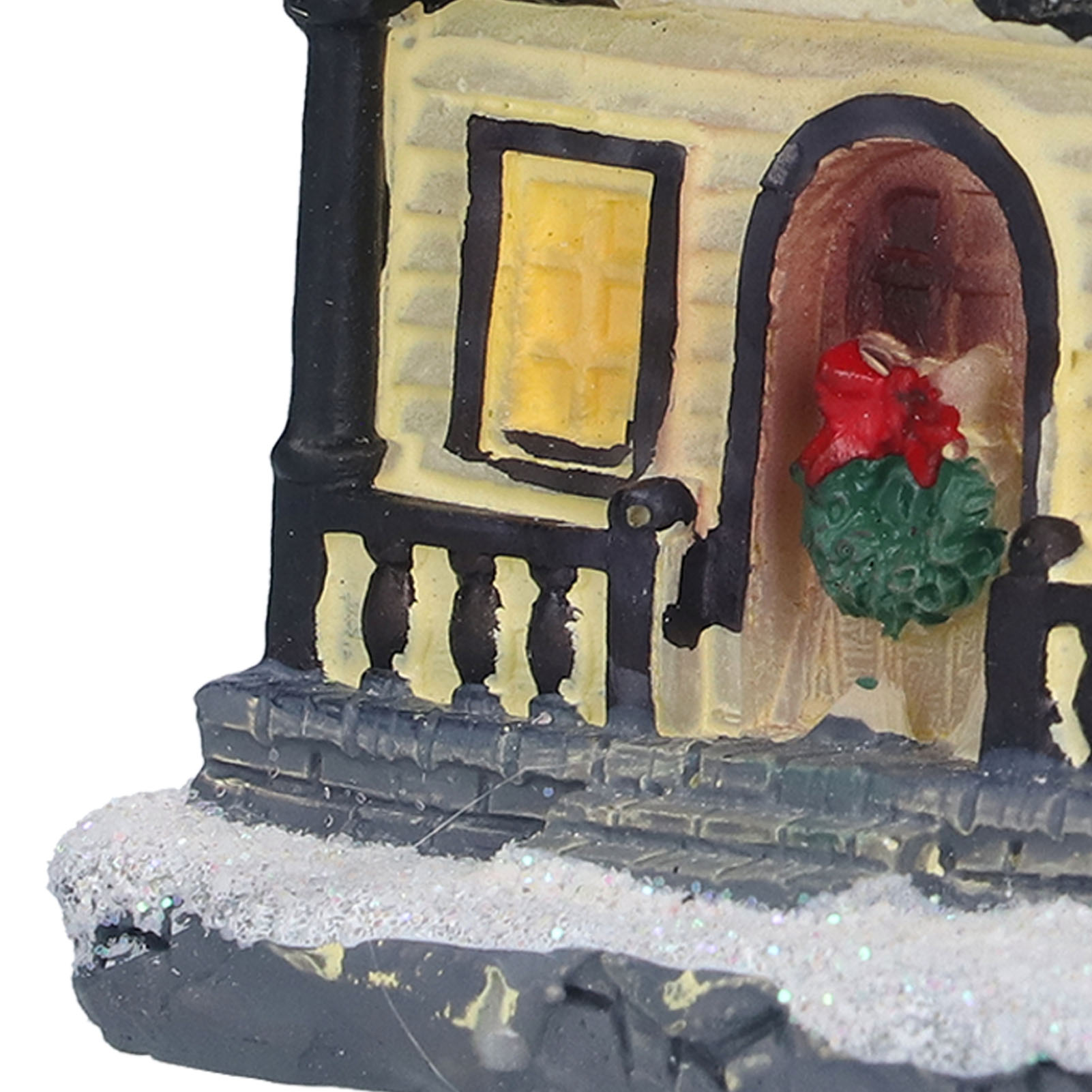 Ein Miniaturhaus mit einem grünen Kranz und einer roten Schleife an der Tür. Gelbes Fenster und schneebedeckte Basis.