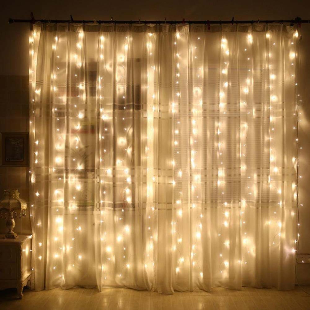 Transparente weiße Vorhänge mit Lichterketten. Eine Lampe links und ein Fenster im Hintergrund.