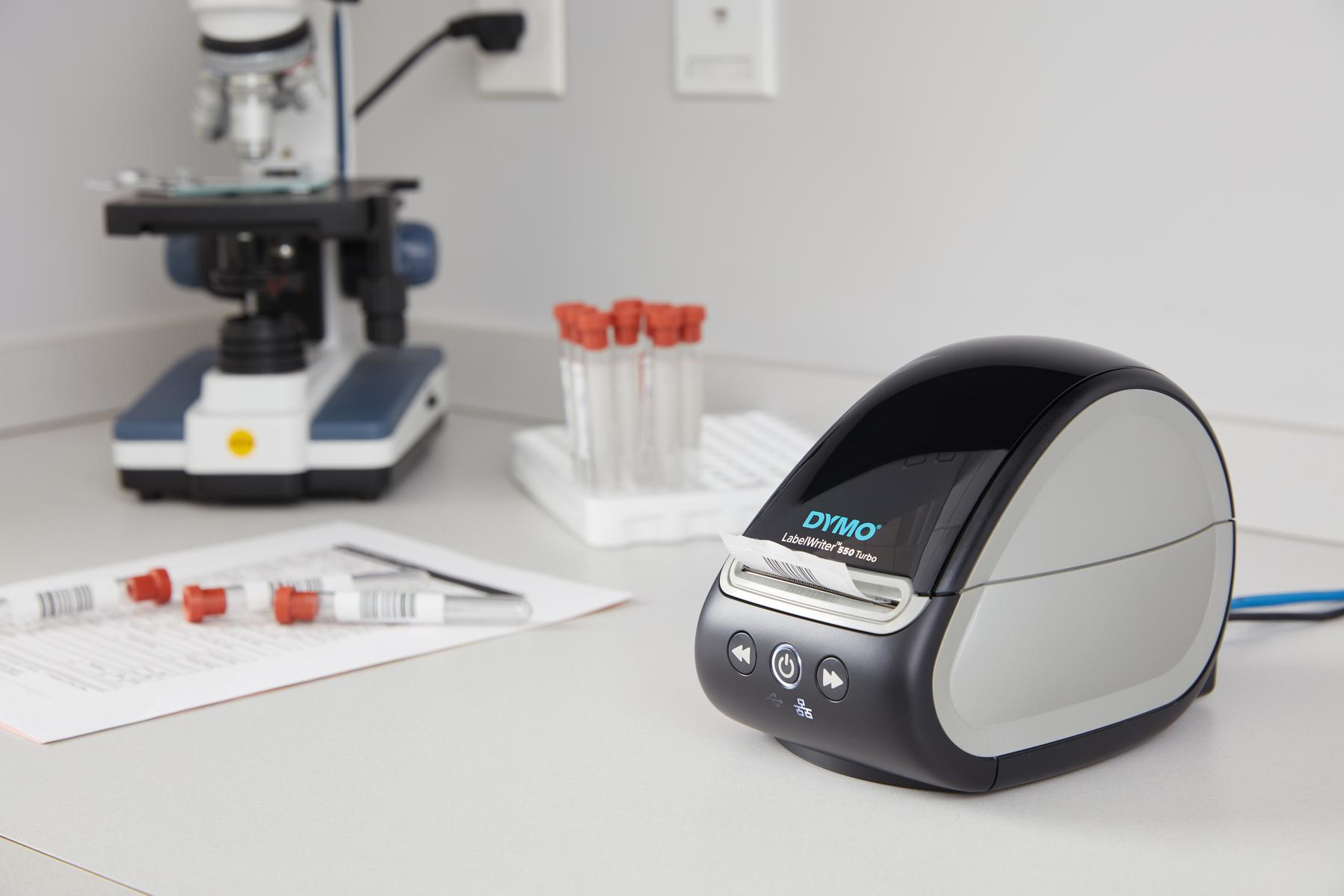 Una Dymo LabelWriter 450 Turbo, un microscopio, provette e documenti sono su un tavolo da laboratorio bianco.
