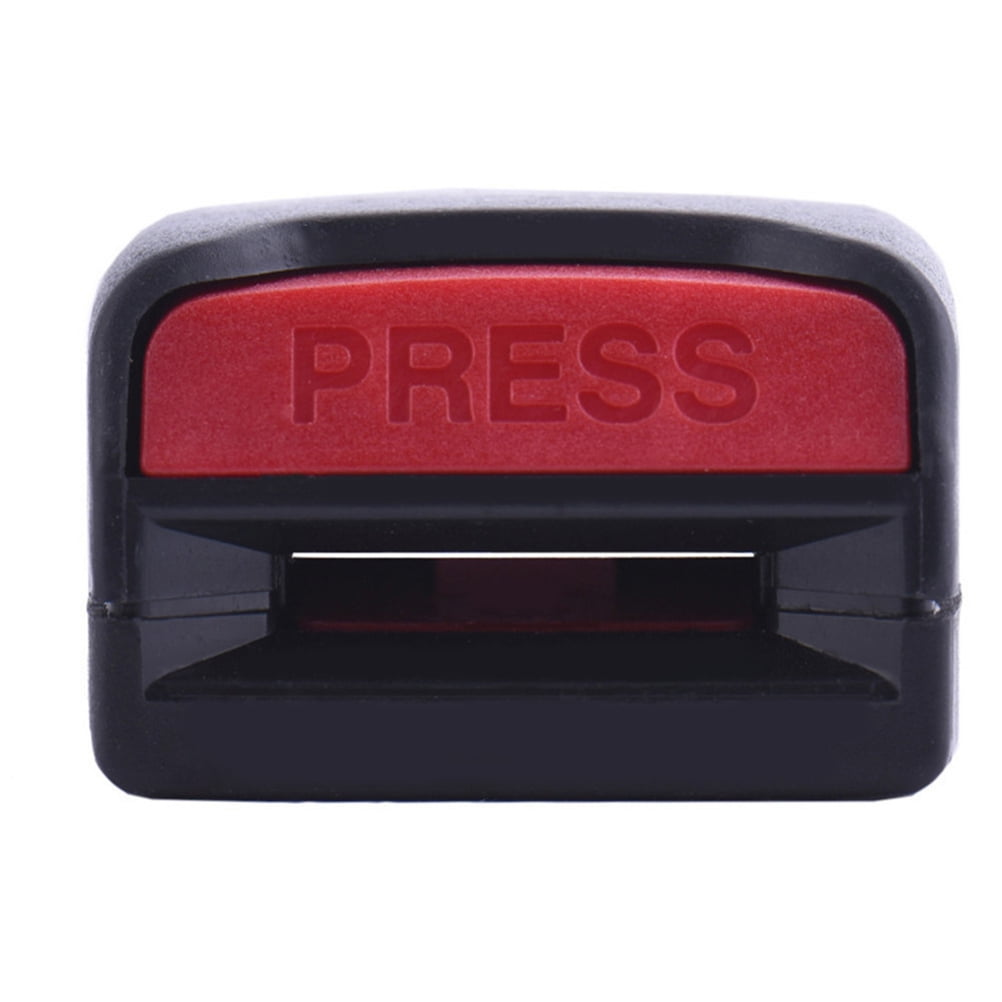 Eine schwarze Autoschnalle mit rotem 'PRESS'-Knopf in der Mitte. Die Schnalle ist rechteckig und hat einen Schlitz.
