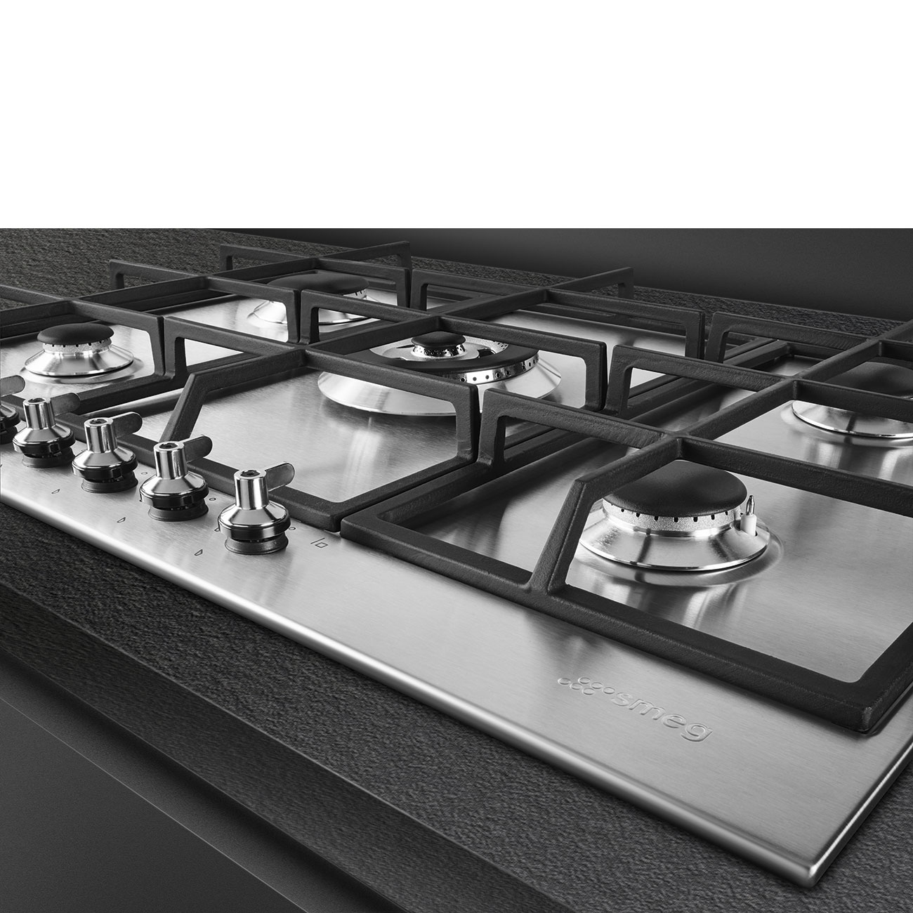 Un piano cottura a gas in acciaio inox con cinque fuochi. Griglie e manopole nere visibili. Il marchio 'smeg' è sulla superficie.