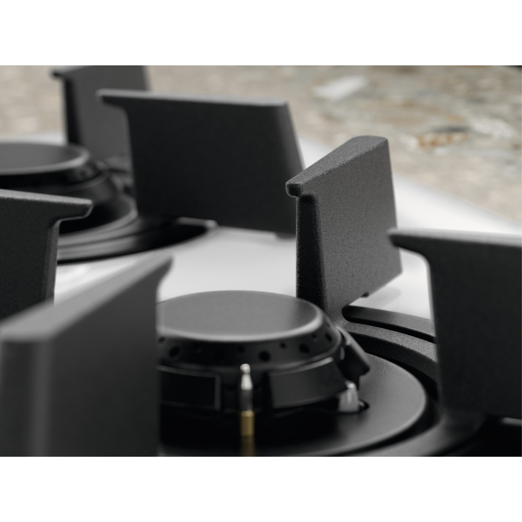 Primo piano di un piano cottura con griglie e bruciatori neri. Lo sfondo è un piano di lavoro di colore chiaro.
