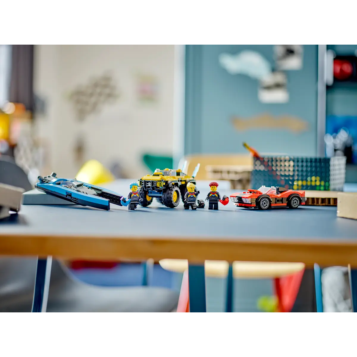 Una scena Lego con una barca blu, un camion giallo, un'auto rossa e minifigure su un tavolo blu. Lo sfondo presenta un muro.
