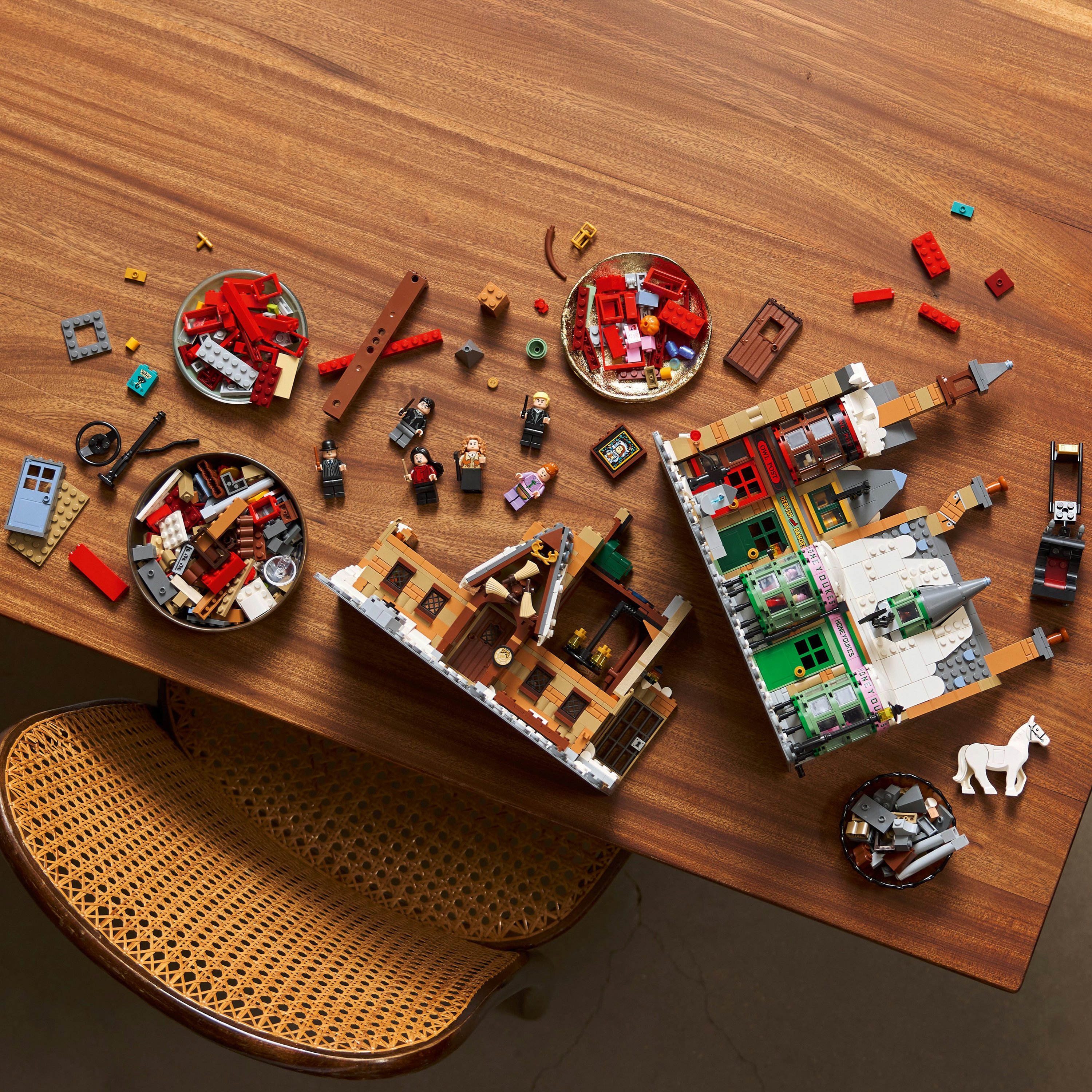 Drewniany stół z klockami Lego, figurkami i sekcjami budynków. Krzesło po lewej stronie.