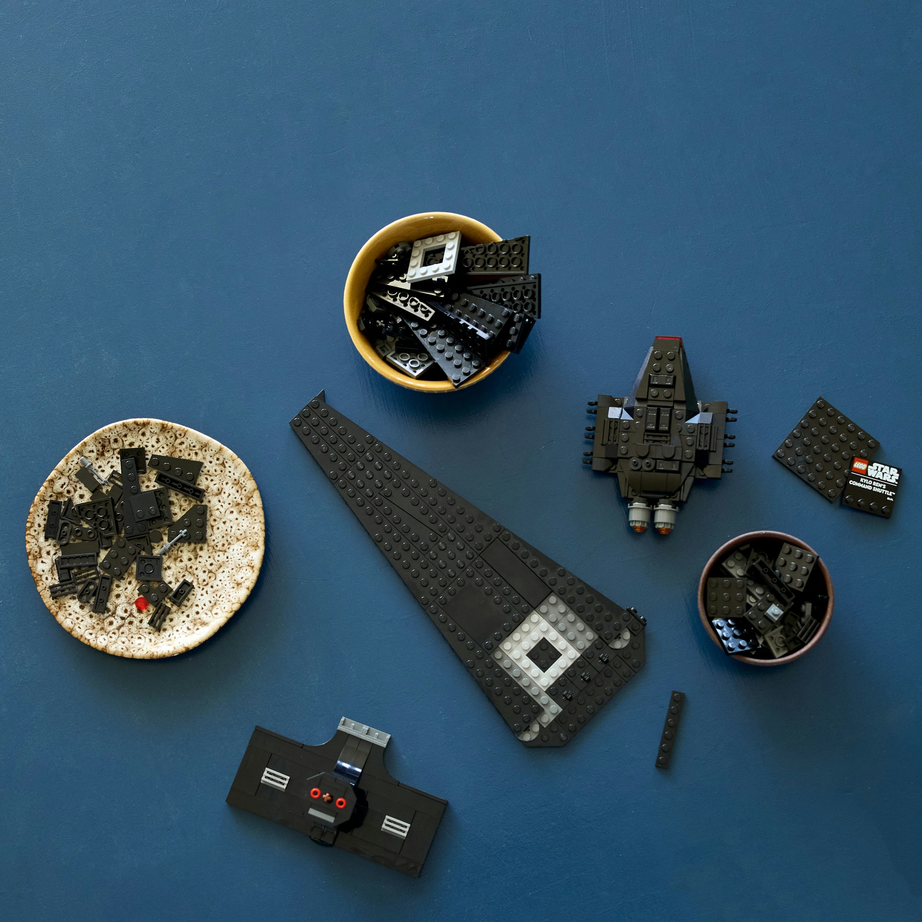 Yukarıdan görünüm Star Wars Lego. Siyah Lego parçaları kaselerde ve monte edilmiş. Ortada büyük bir gemi.