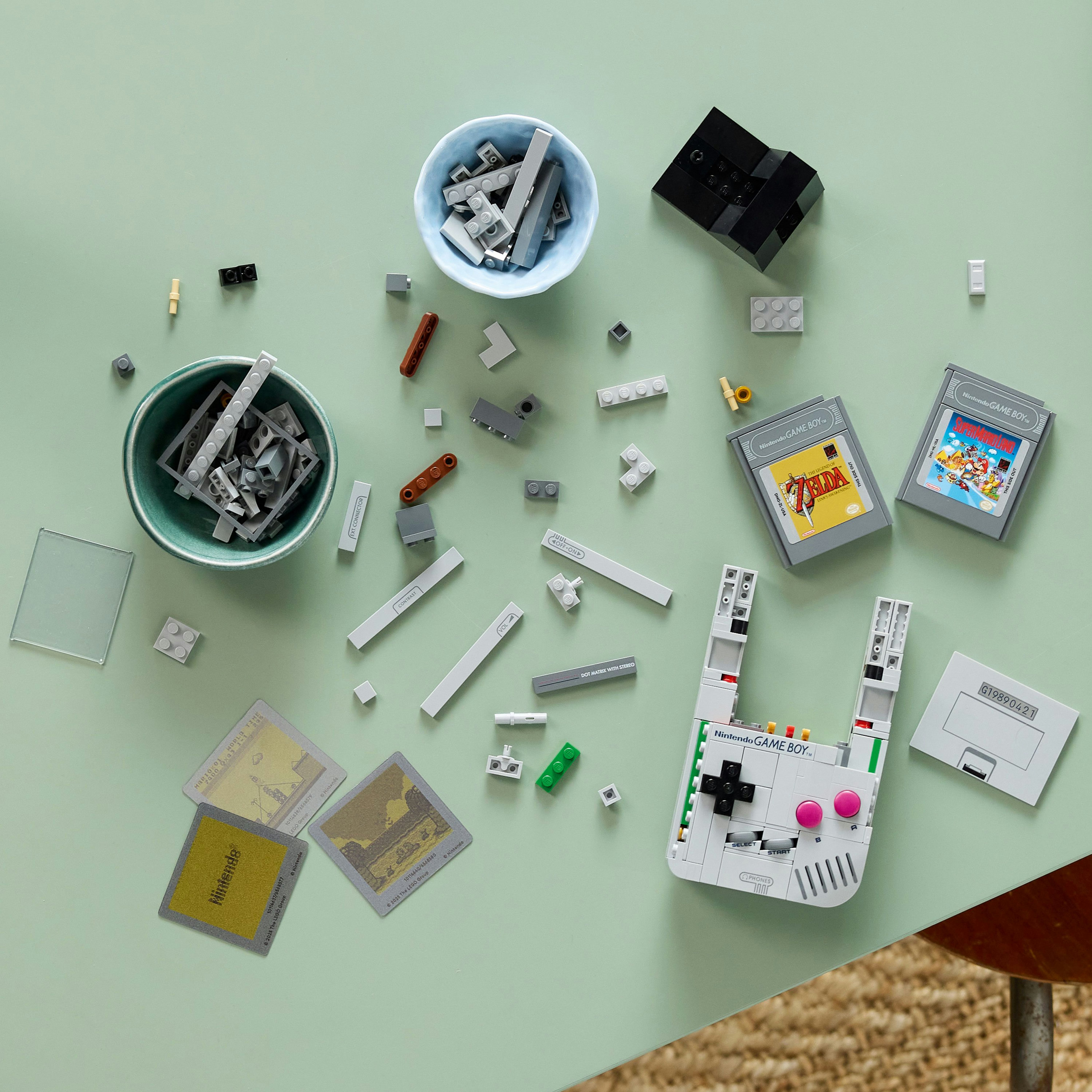 Yeşil bir yüzeyde gevşek tuğlalar, oyun kartuşları ve kaseler ile Lego Game Boy yapımı.