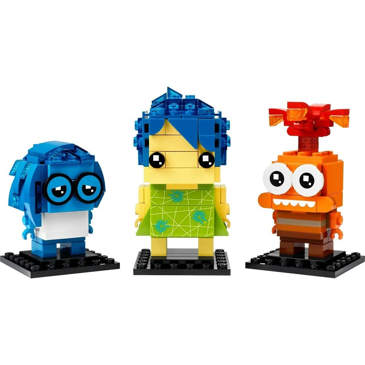 Trois figurines Lego : Tristesse bleue, Joie jaune avec robe verte, et Colère orange. Toutes sur des socles noirs.
