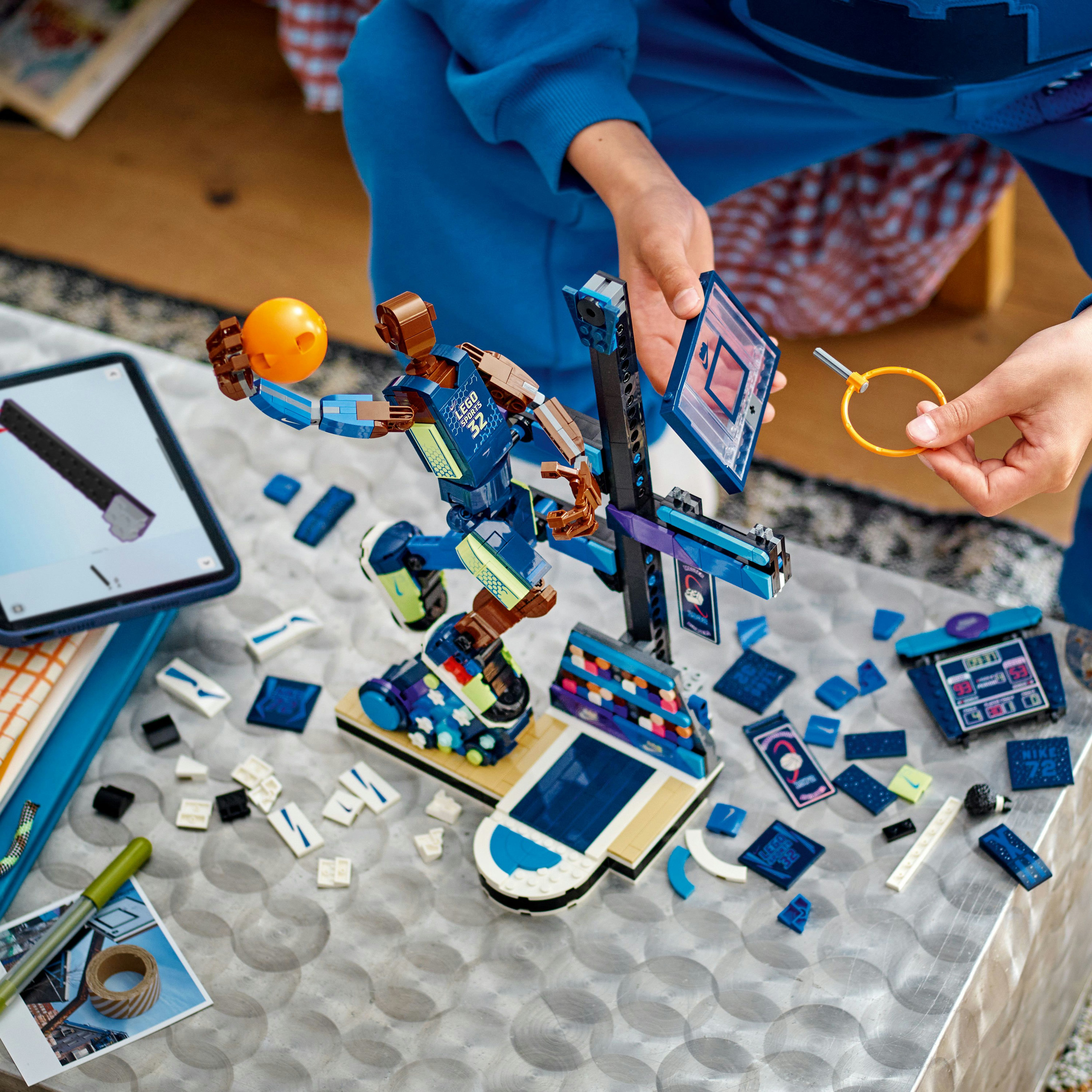 Una persona costruisce un giocatore di basket LEGO. Il giocatore tiene una palla. Pezzi LEGO sparsi e un tablet sono sul tavolo.
