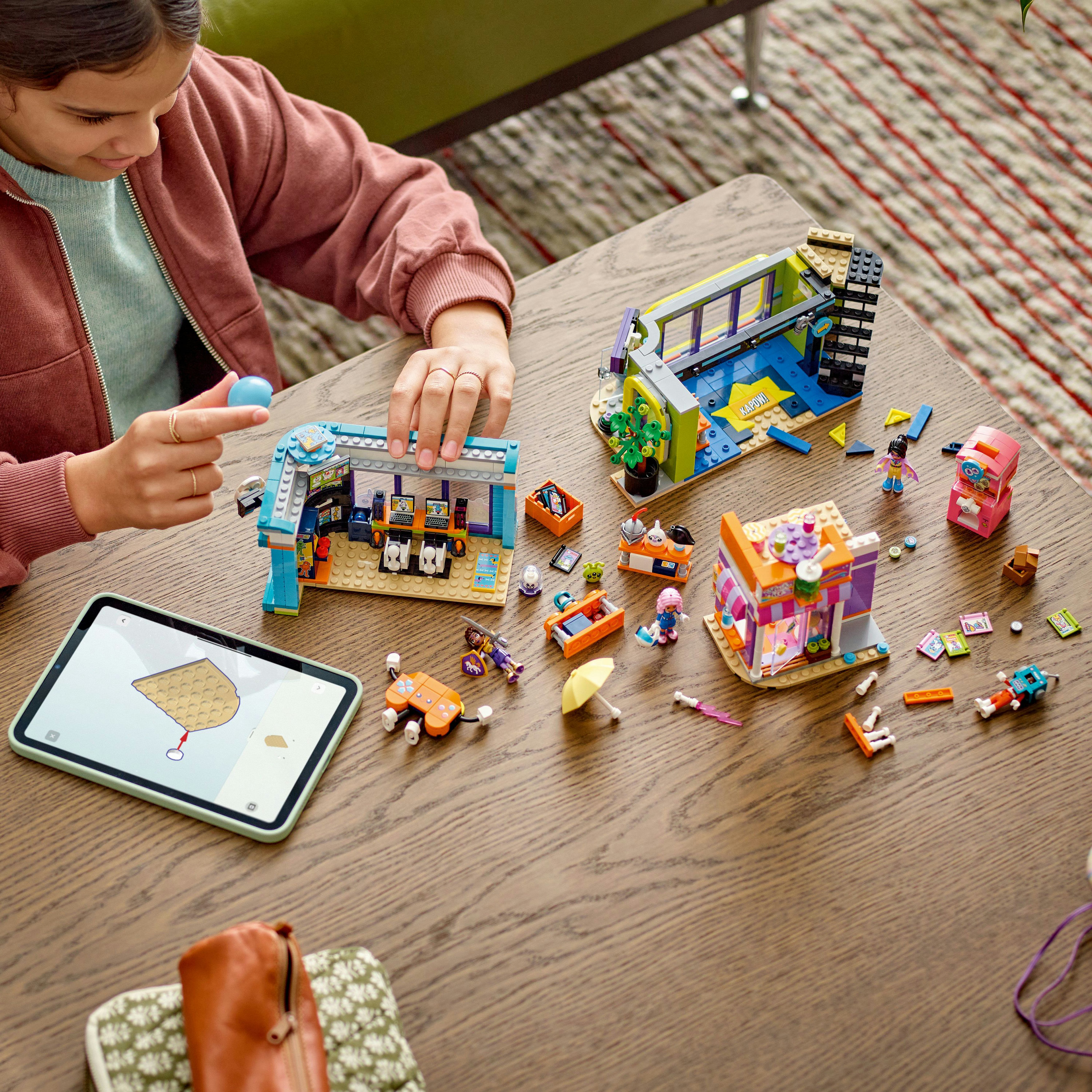 Una persona sta giocando con set Lego su un tavolo di legno. Ci sono diverse strutture Lego, personaggi e un tablet con istruzioni.