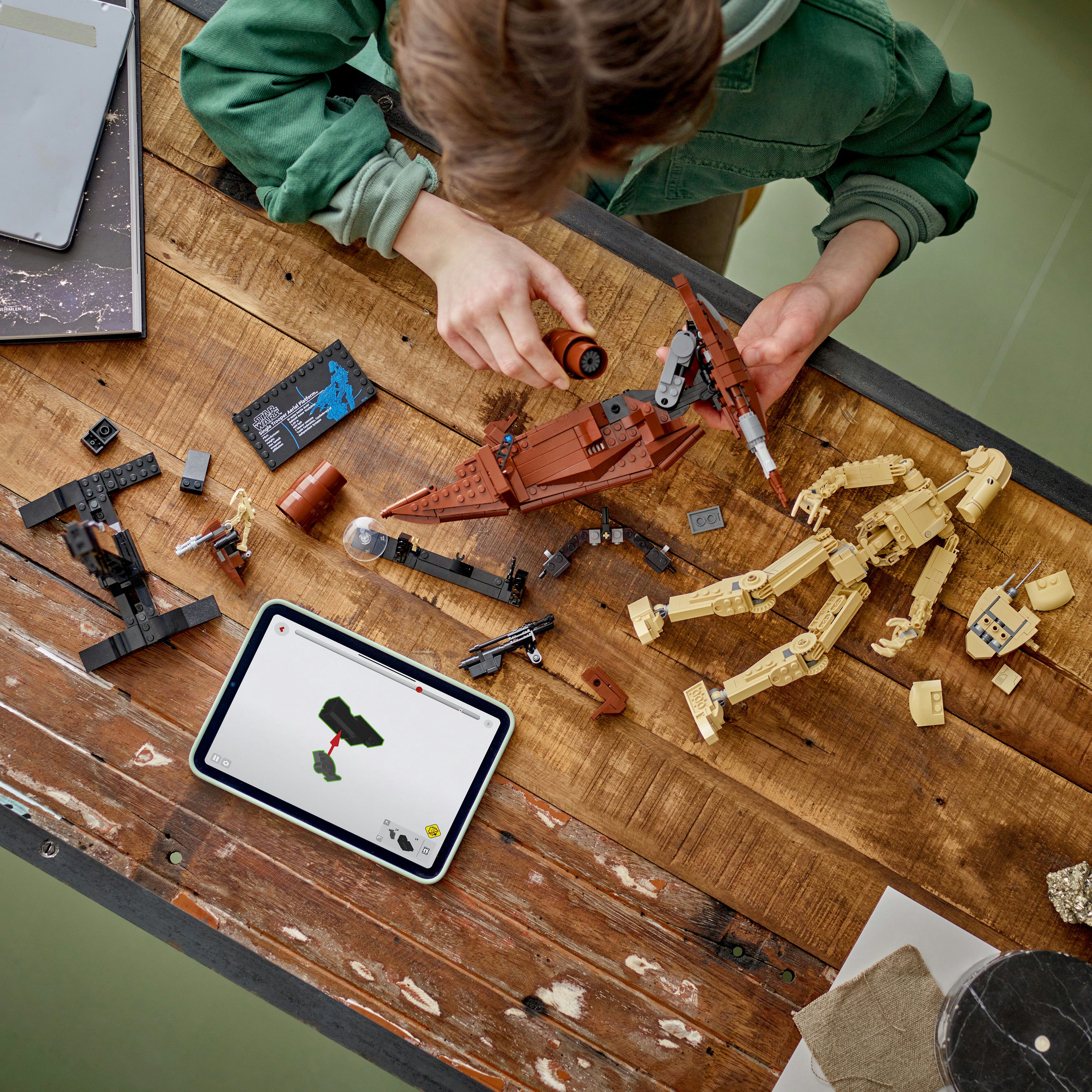 Osoba składająca zestaw Lego. Części zestawu i tablet z instrukcjami leżą na drewnianym stole.
