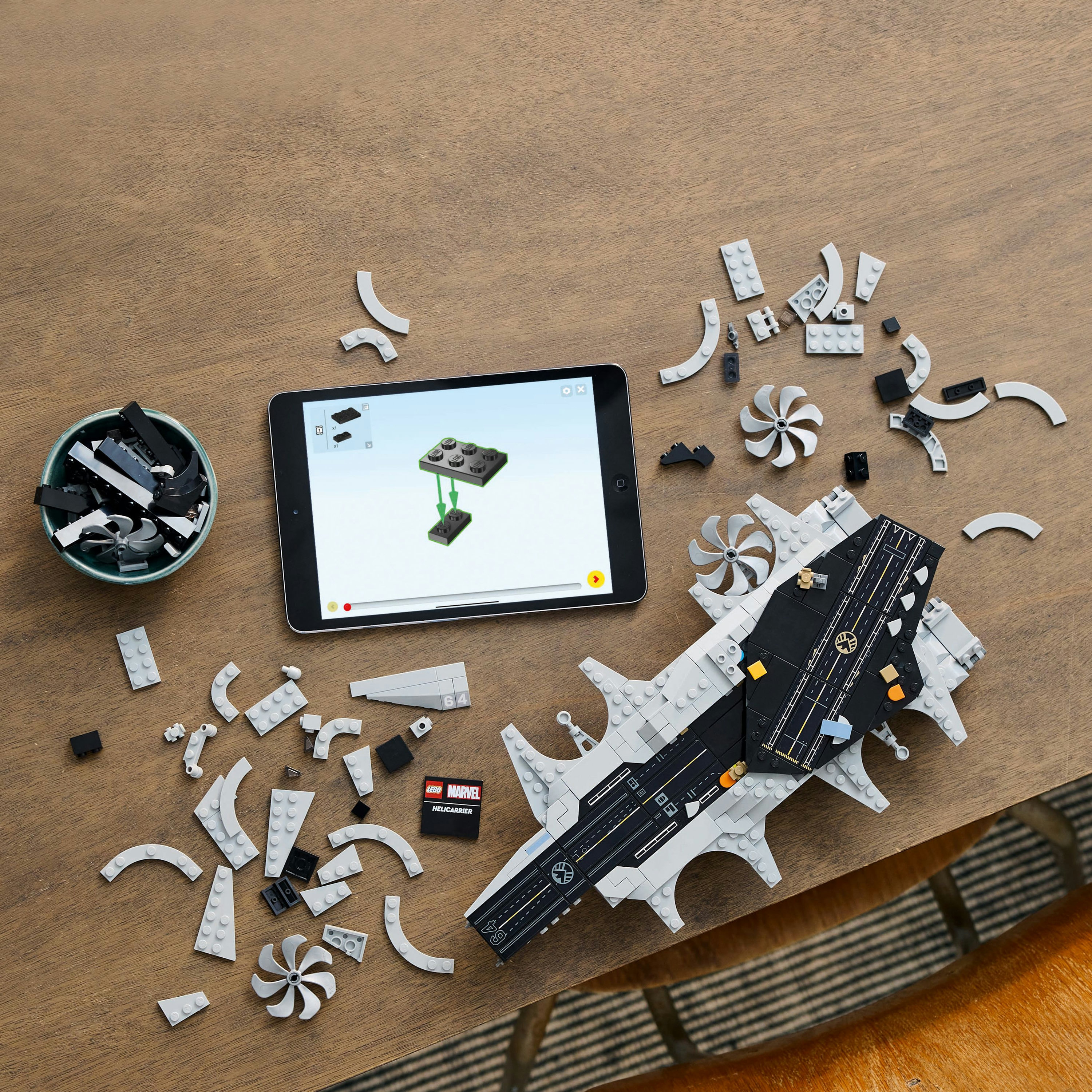 Set Lego Marvel Helicarrier con pezzi sparsi, istruzioni su tablet e una ciotola di mattoncini Lego neri.
