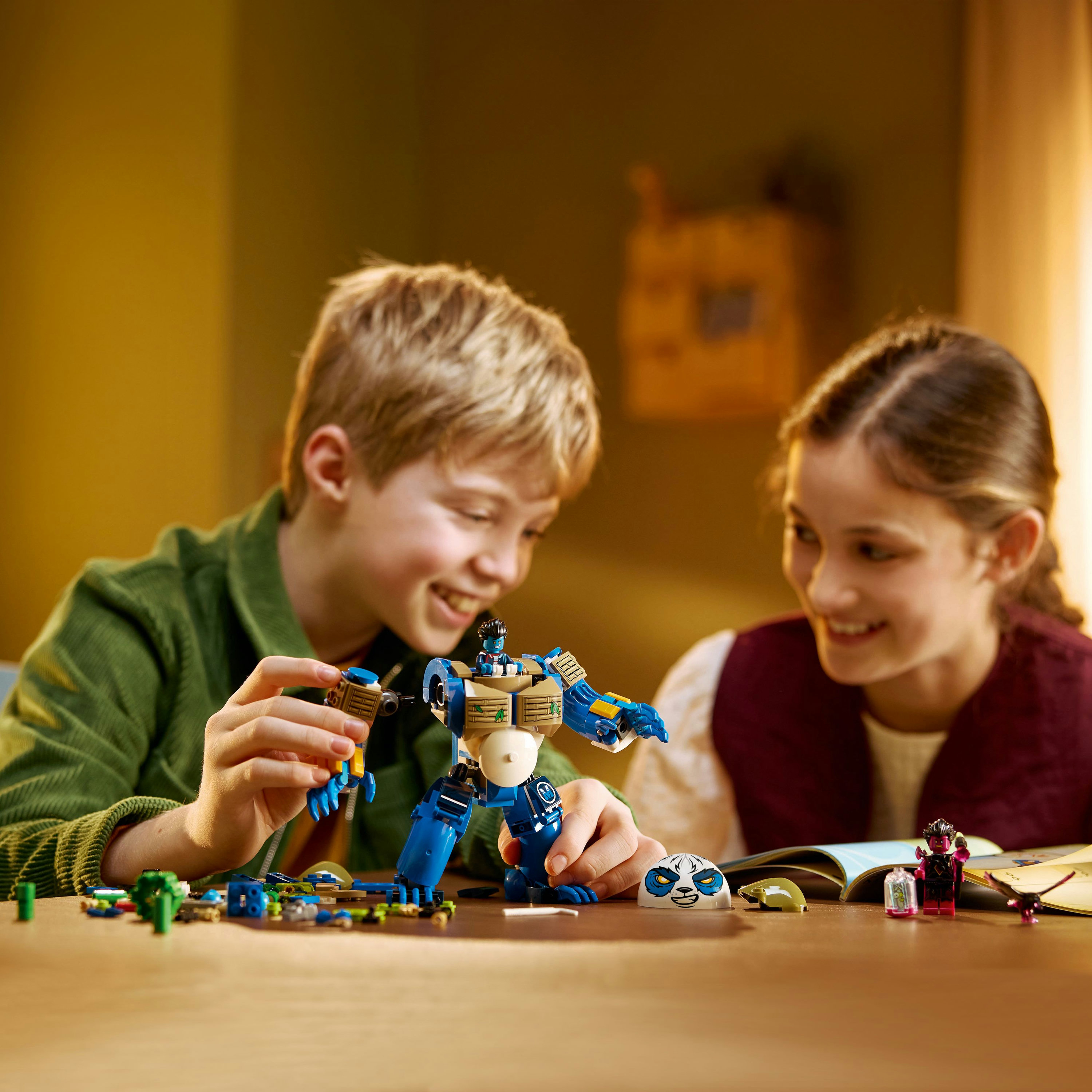 Deux enfants souriants construisent un robot bleu avec des briques Lego sur une table en bois. Pièces et instructions Lego visibles.