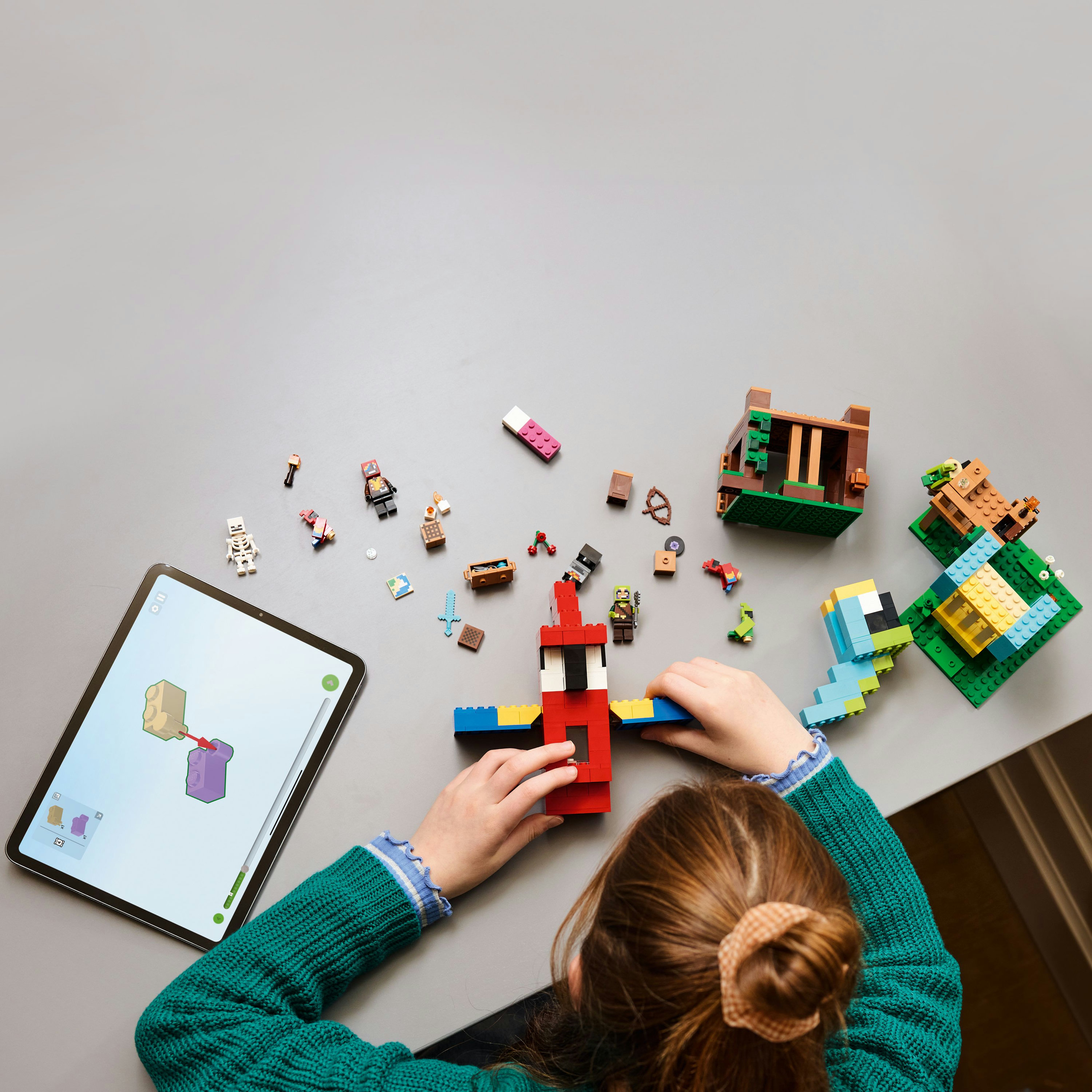 Dziecko buduje zestaw Lego Minecraft na stole. Tablet wyświetla instrukcje. W pobliżu znajdują się różne elementy i figurki.