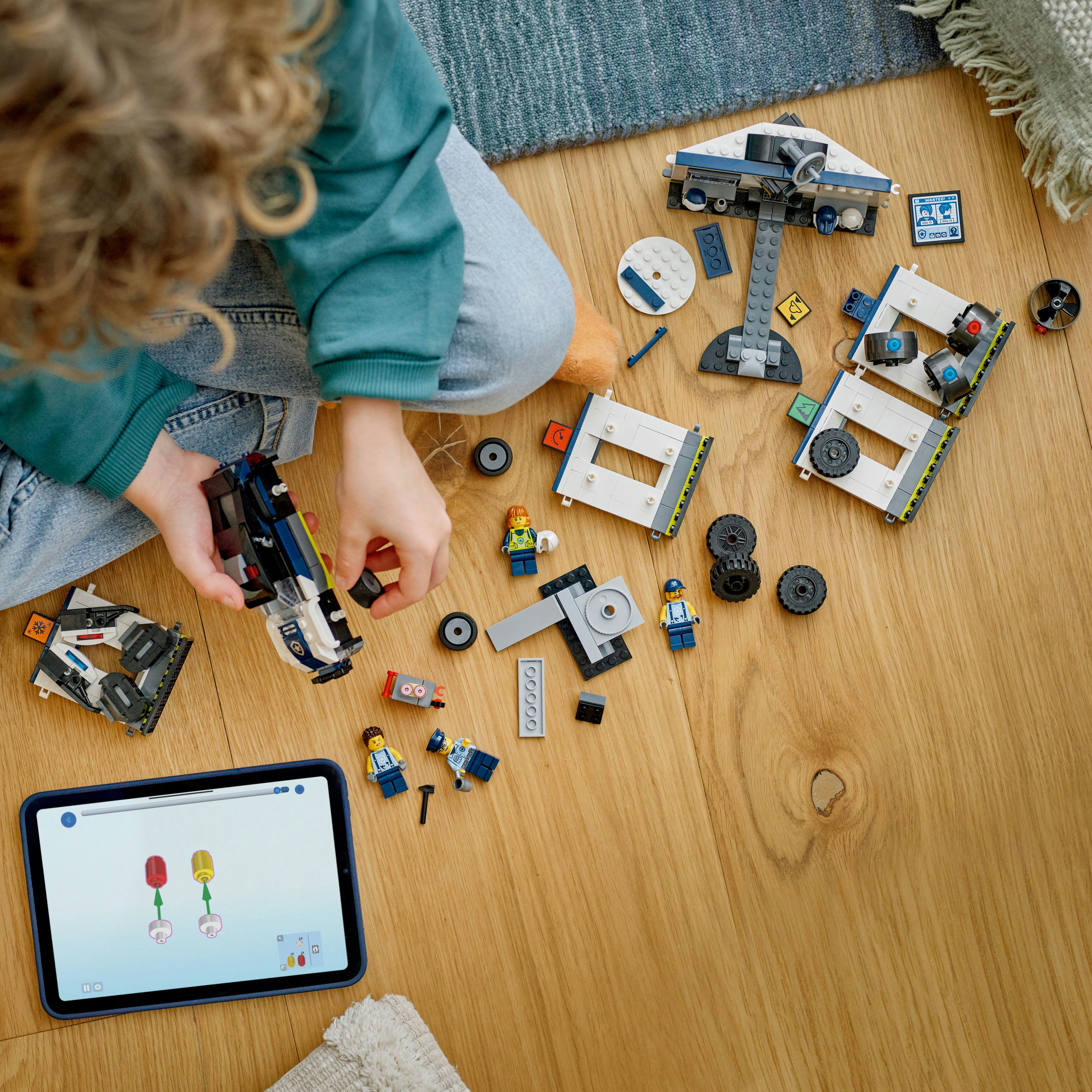 Dziecko bawi się zestawami Lego posterunku policji na drewnianej podłodze. Tablet wyświetla instrukcje budowy. Różne klocki Lego.