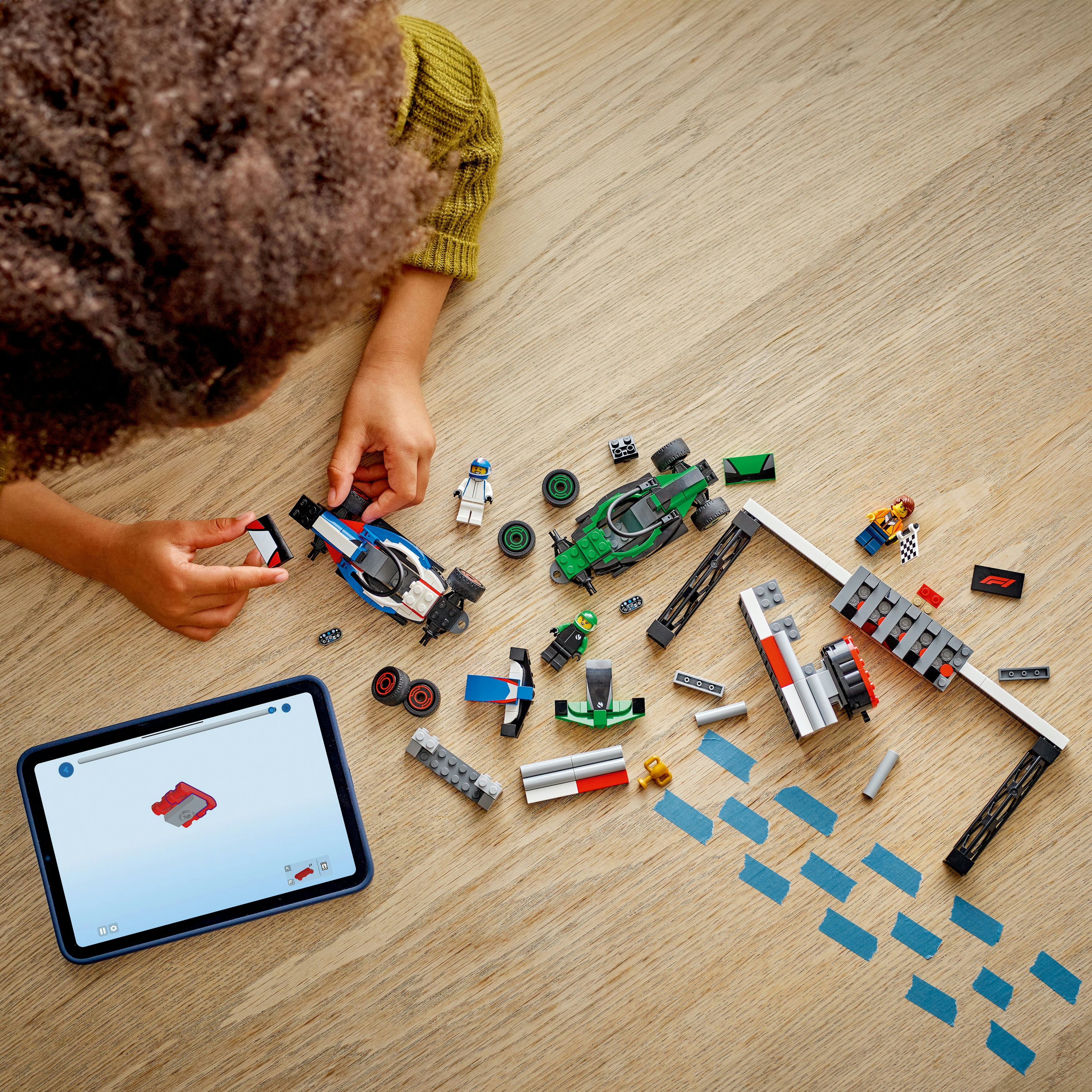 Dziecko składa samochód wyścigowy LEGO na drewnianej powierzchni z tabletem wyświetlającym instrukcje. Różne elementy LEGO są rozrzucone.