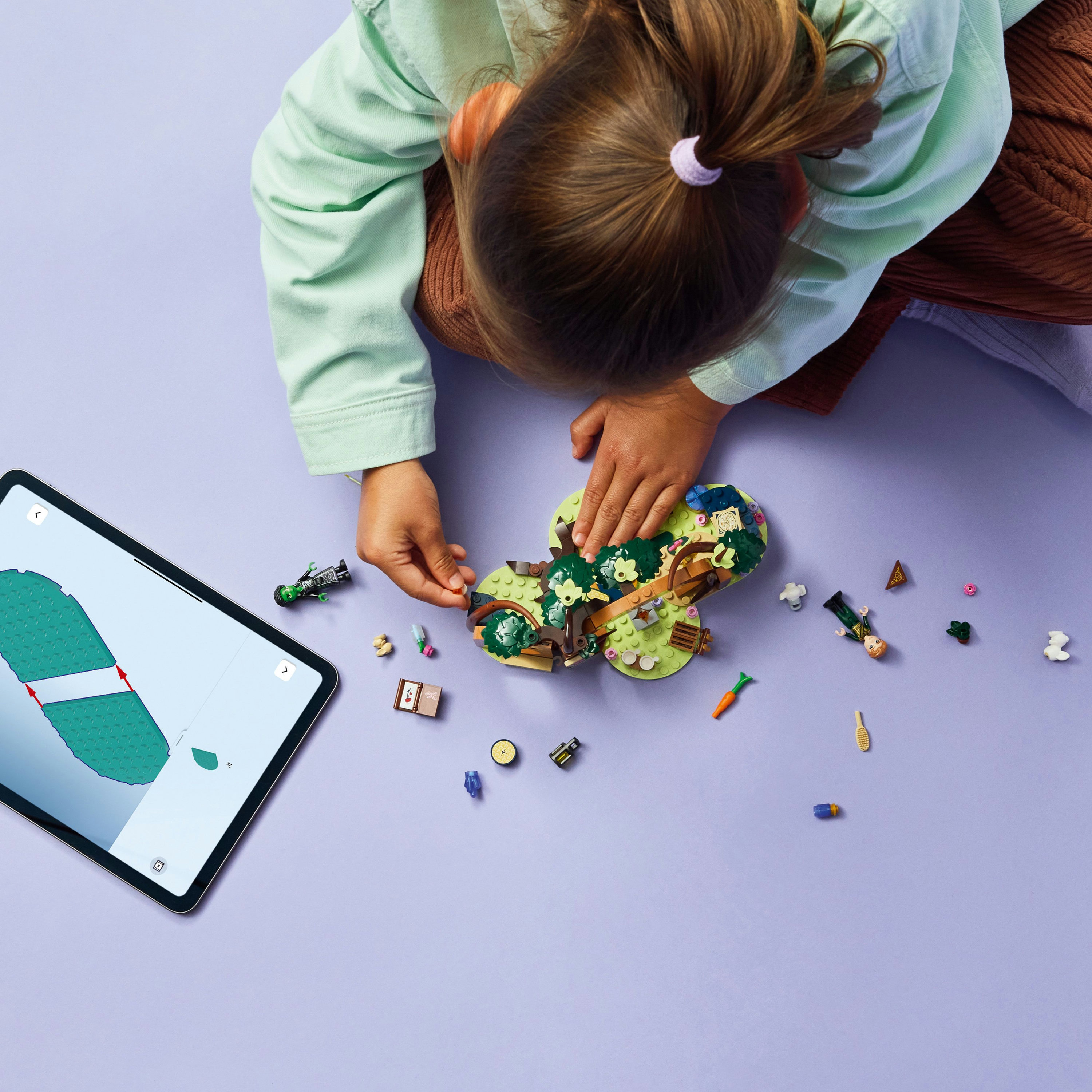 Dziecko składa zestaw Lego. Tablet wyświetla instrukcje. Różne elementy Lego są rozrzucone na fioletowej powierzchni.