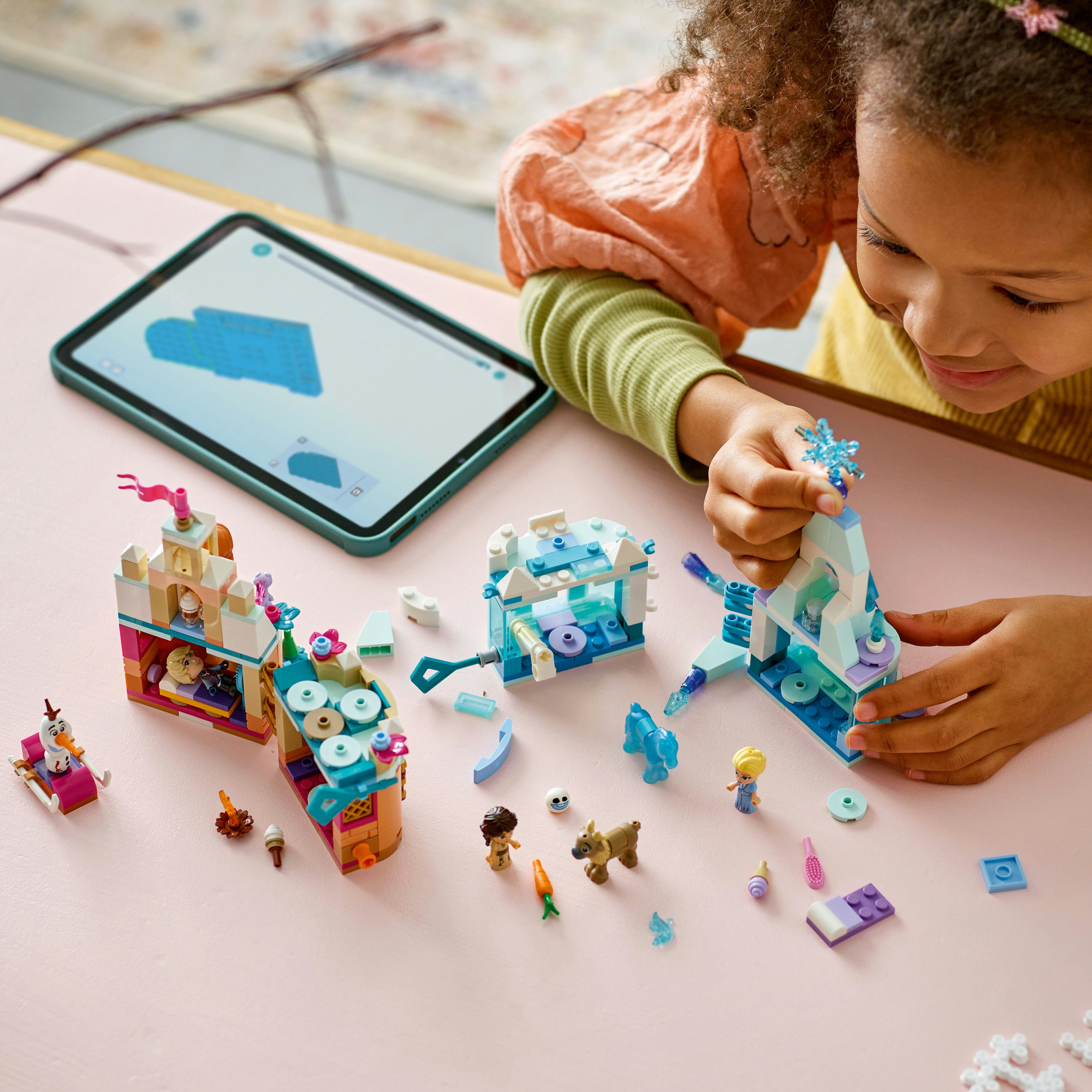 Un bambino gioca con i mattoncini su una superficie rosa. Ci sono personaggi Lego e un tablet.