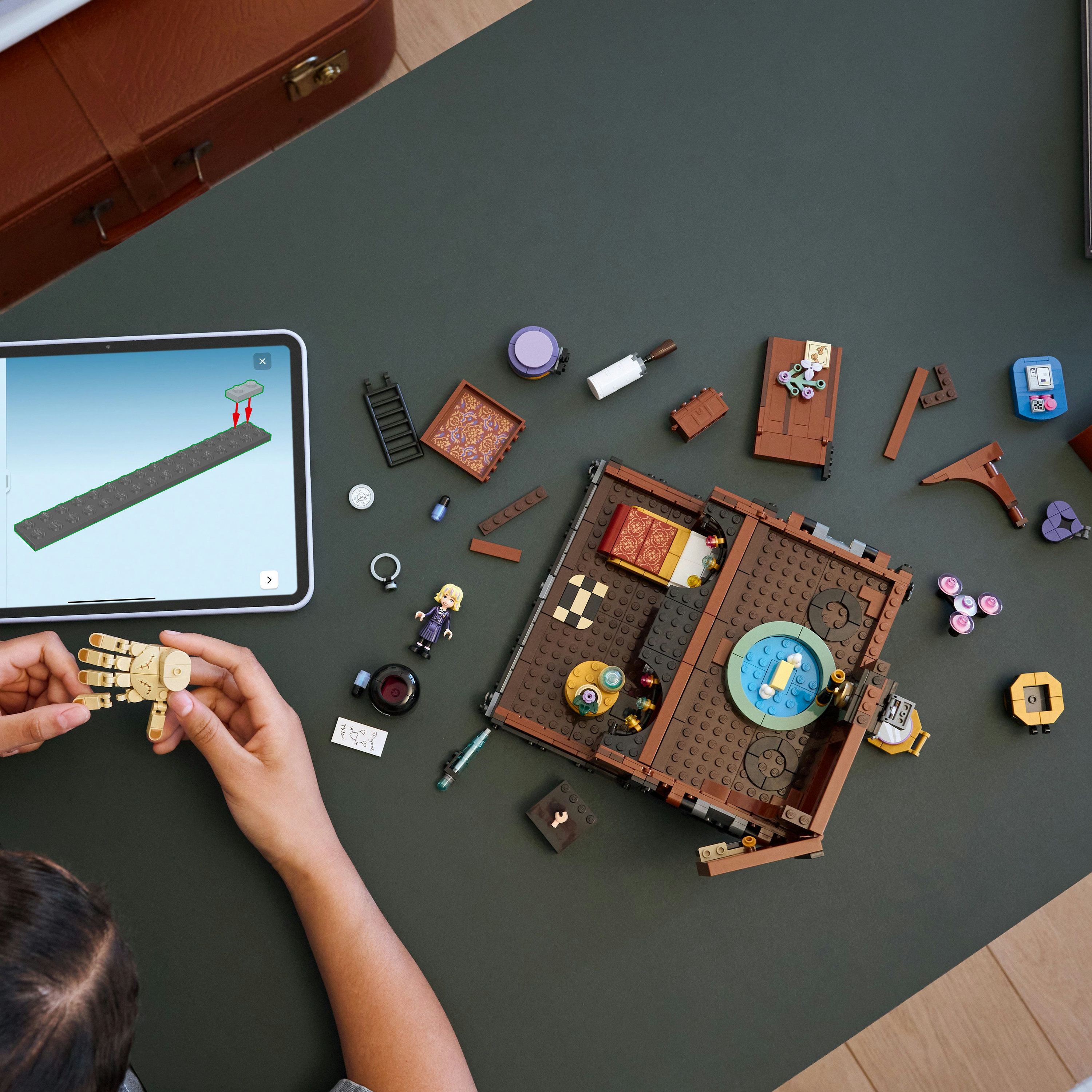 Osoba składa zestaw Lego. Zestaw przedstawia pokój z różnymi klockami Lego rozrzuconymi.