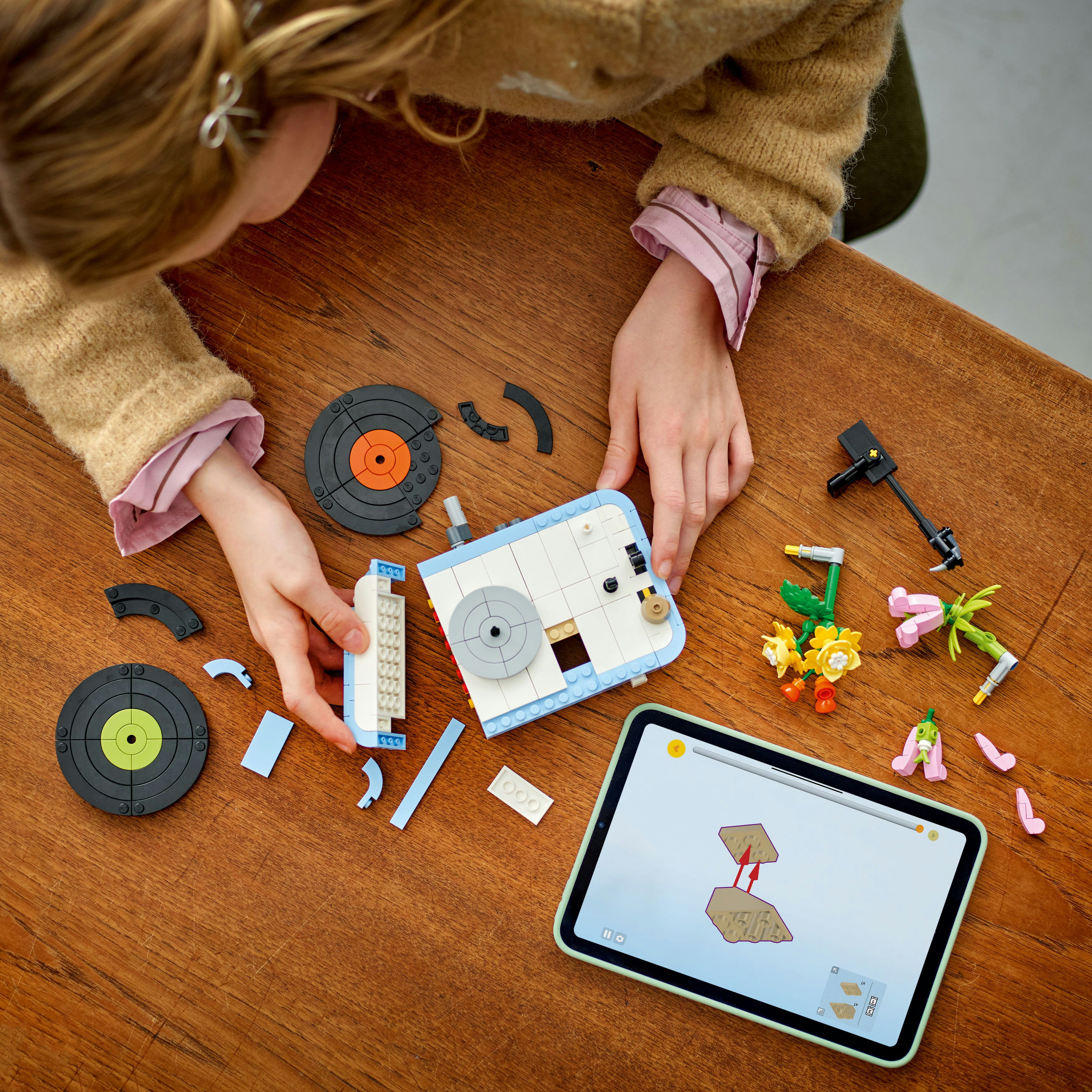 Bir çocuk, ahşap bir masa üzerinde bir müzik çalar Lego seti topluyor, talimatları gösteren bir tablet ile.
