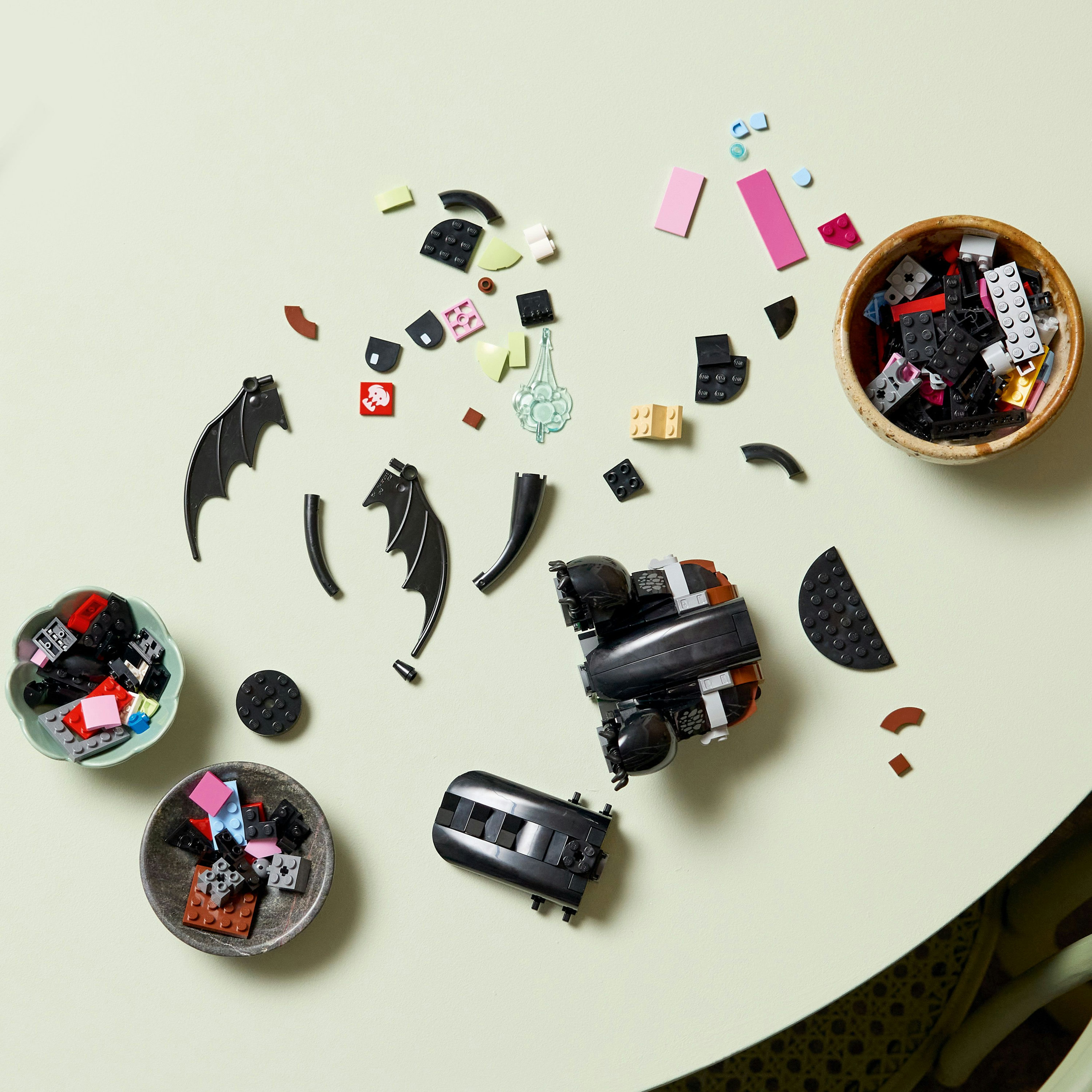 Rozrzucone klocki LEGO i miski w różnych kolorach na jasnozielonej powierzchni. Części modelu są montowane.