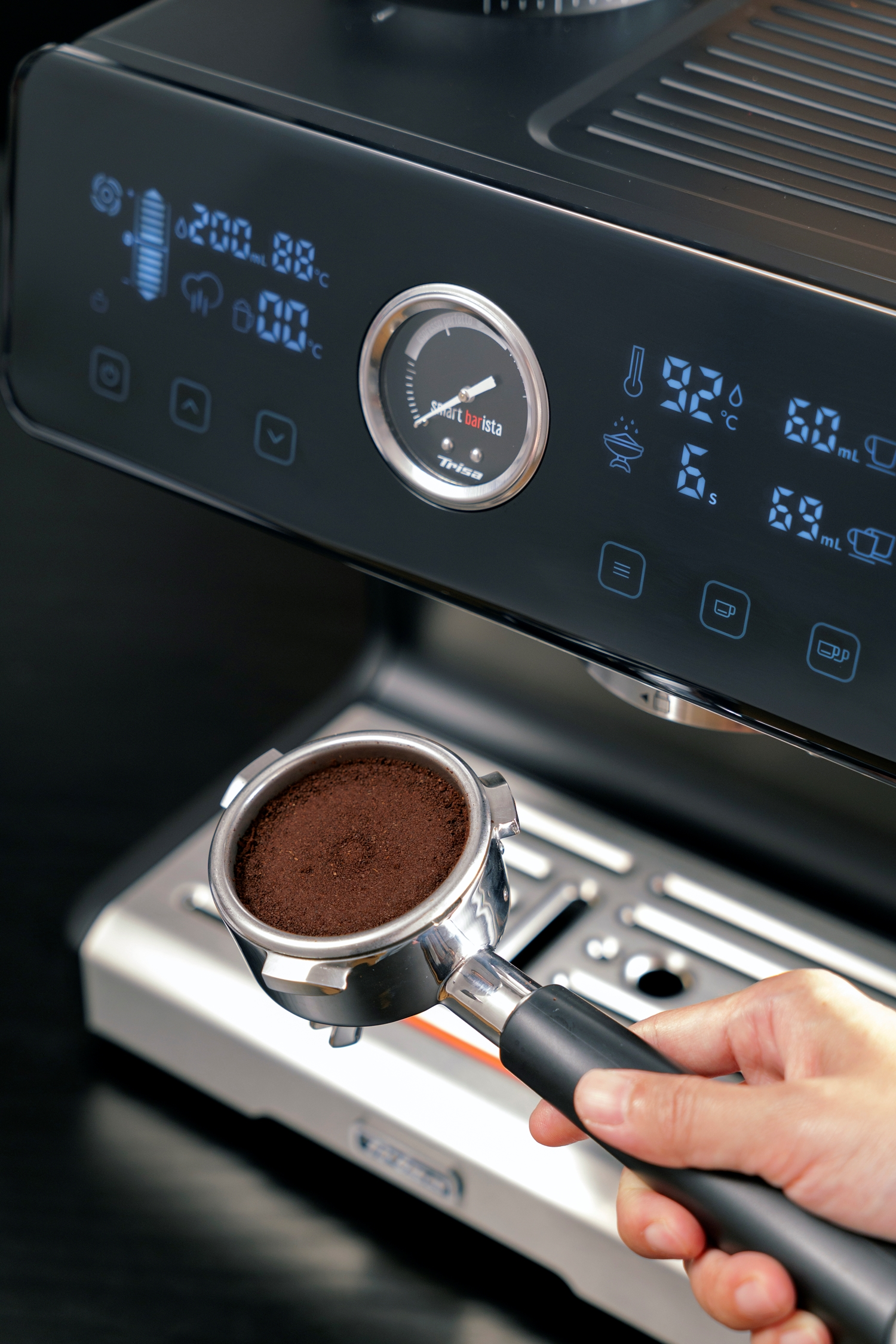 Eine Hand hält einen Siebträger mit Kaffeepulver vor einer schwarzen Espressomaschine. Das Display der Maschine zeigt Einstellungen.