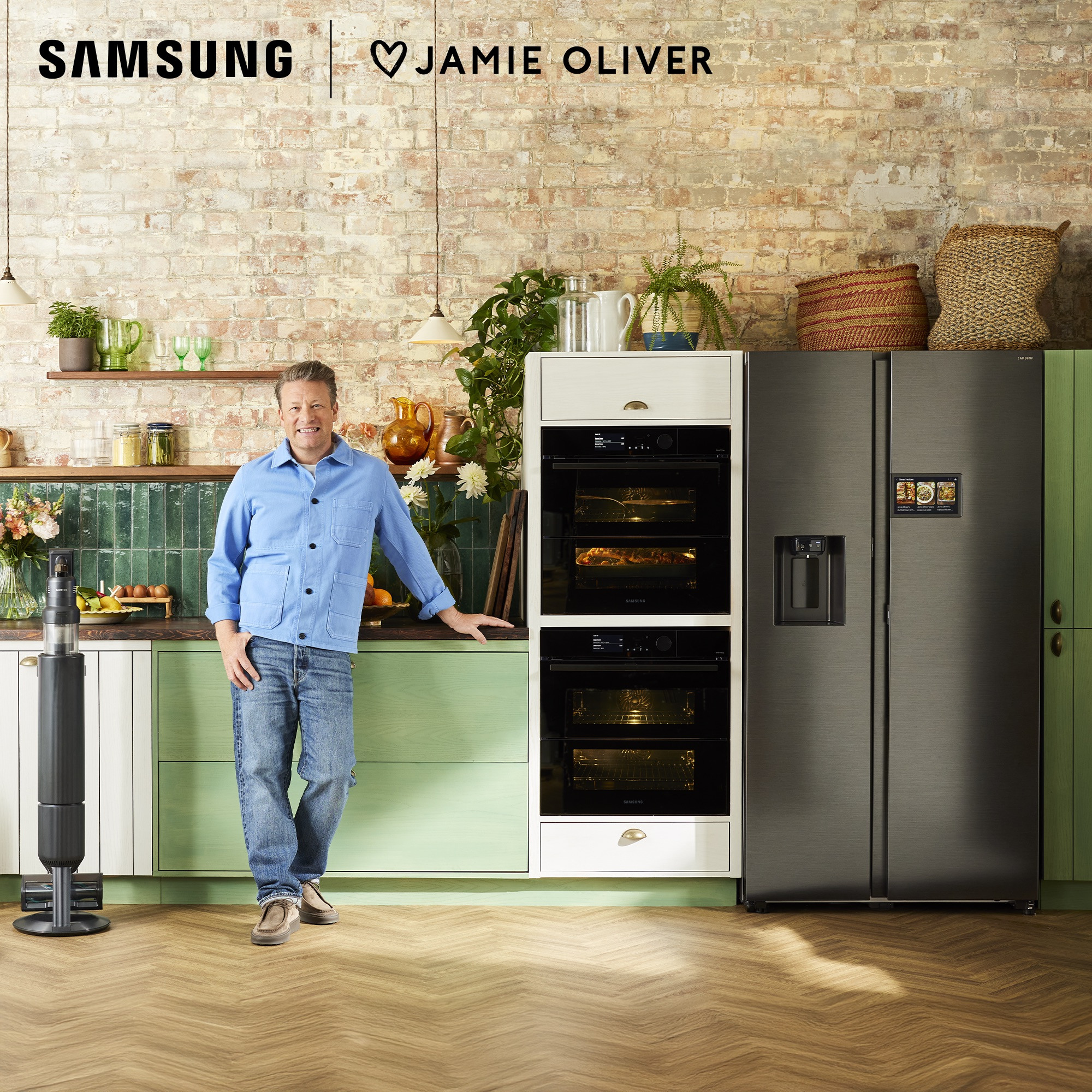 Jamie Oliver, Samsung cihazlı bir mutfakta. Tuğla duvar, yeşil ve beyaz dolaplar ve siyah bir buzdolabı görülüyor.