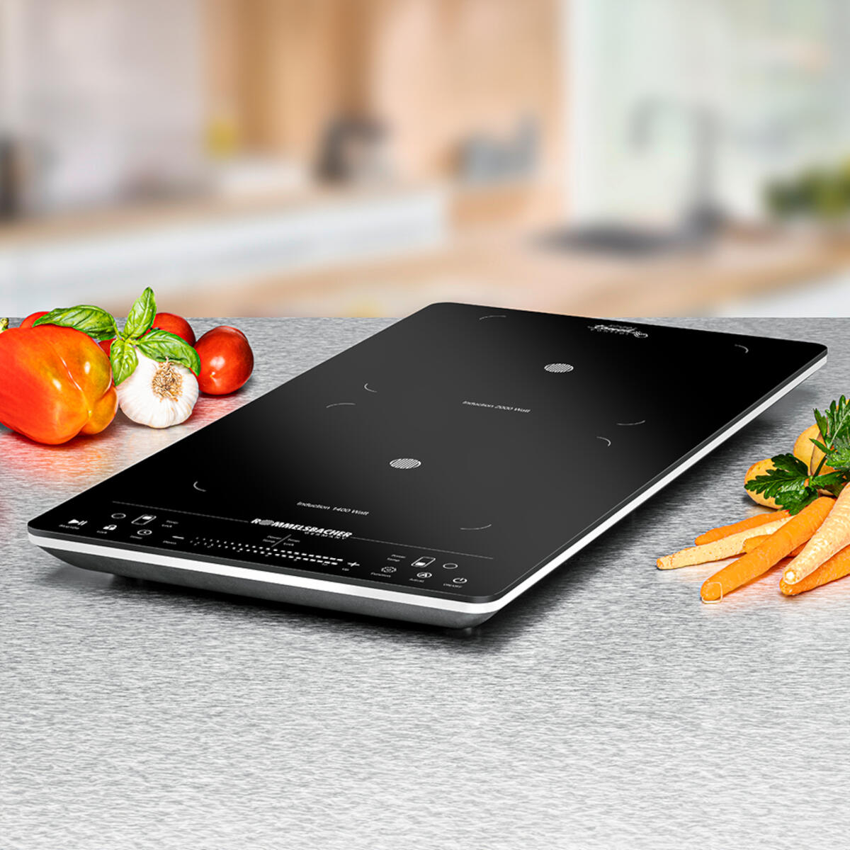 A black induction cooktop with vegetables on a table. Bell pepper, garlic, tomatoes, and carrots are visible.