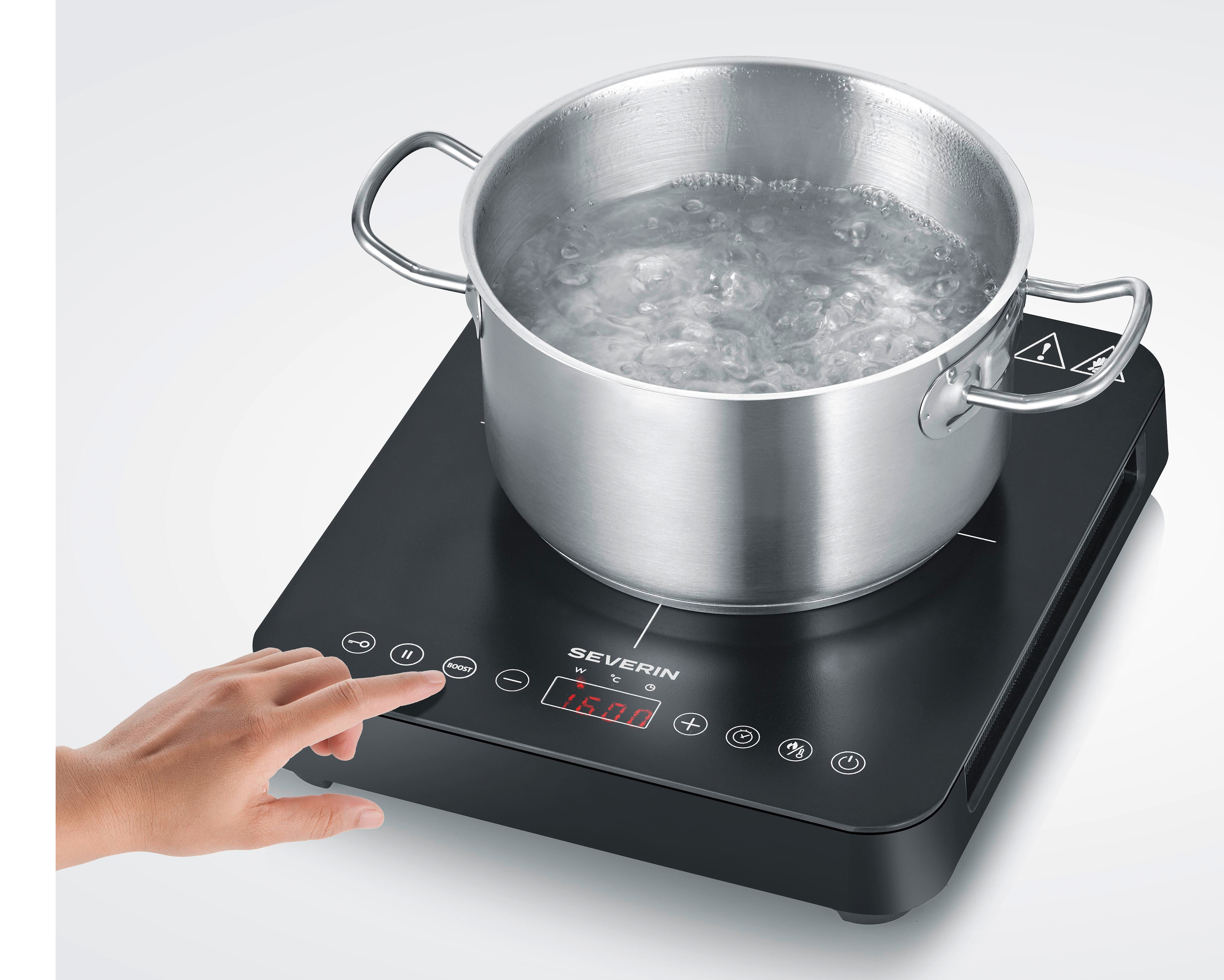 Ręka naciska przycisk na płycie indukcyjnej. Garnek z wrzącą wodą stoi na płycie.