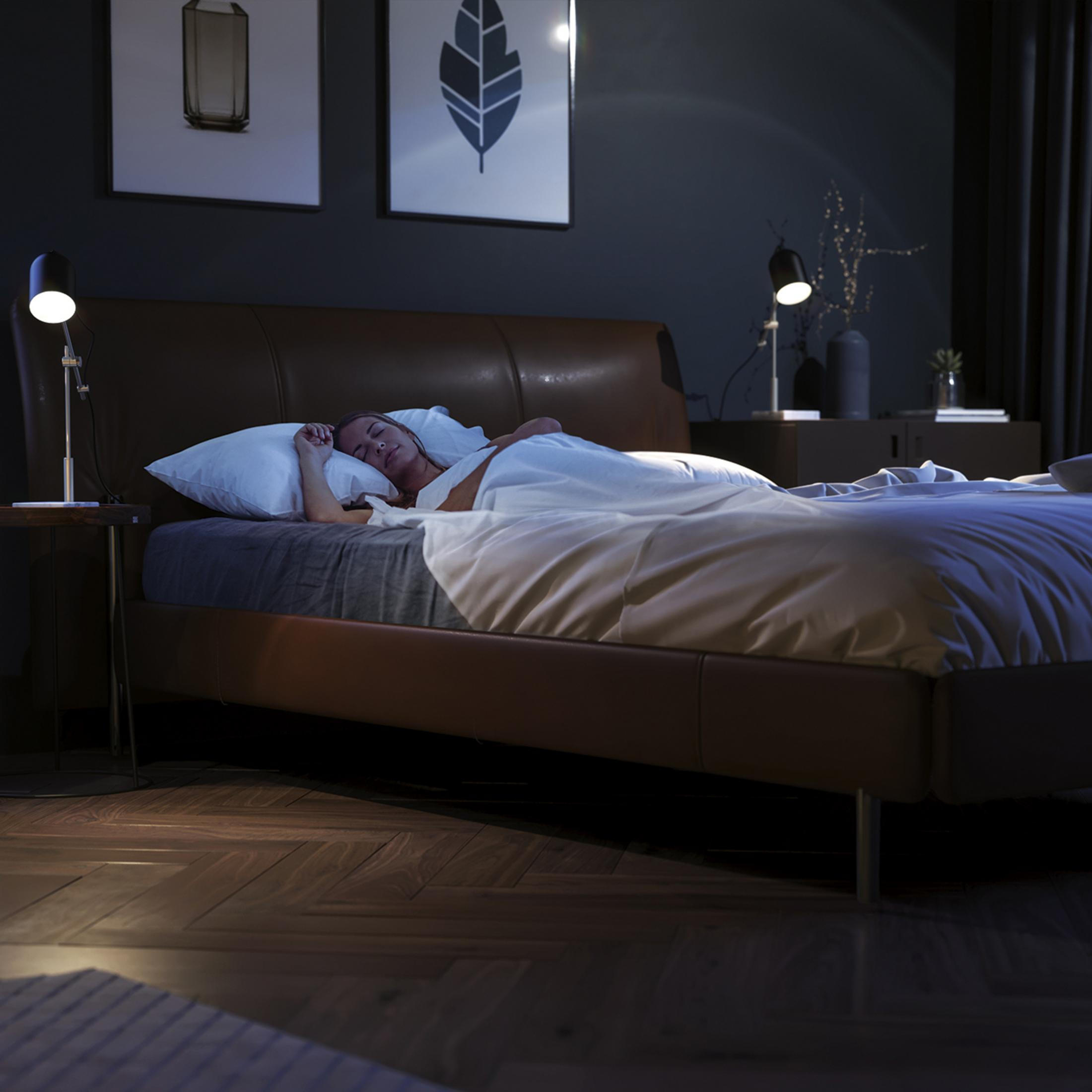 Eine Frau schläft in einem braunen Bett. Lampen, Kunst und ein Nachttisch sind auf beiden Seiten.