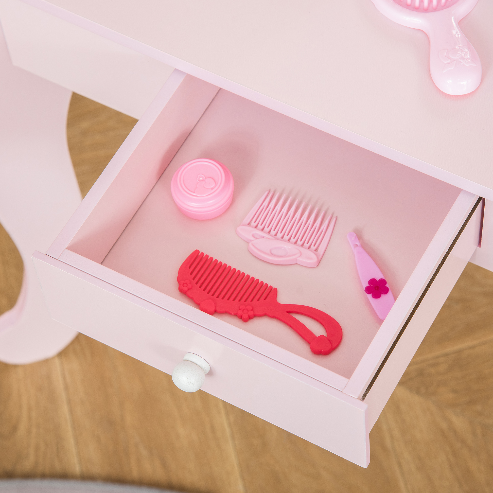 Cajón de tocador de juguete rosa con accesorios: peine, cepillo y tarro de crema. Piso de madera visible.