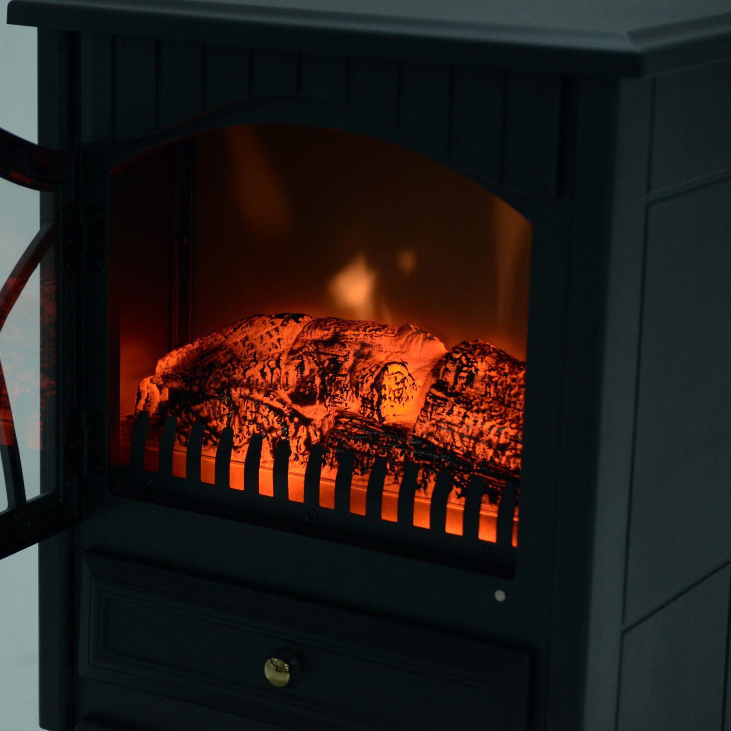 Una chimenea eléctrica negra con un efecto de fuego naranja brillante, puerta de vidrio abierta y un cajón con pomo dorado.